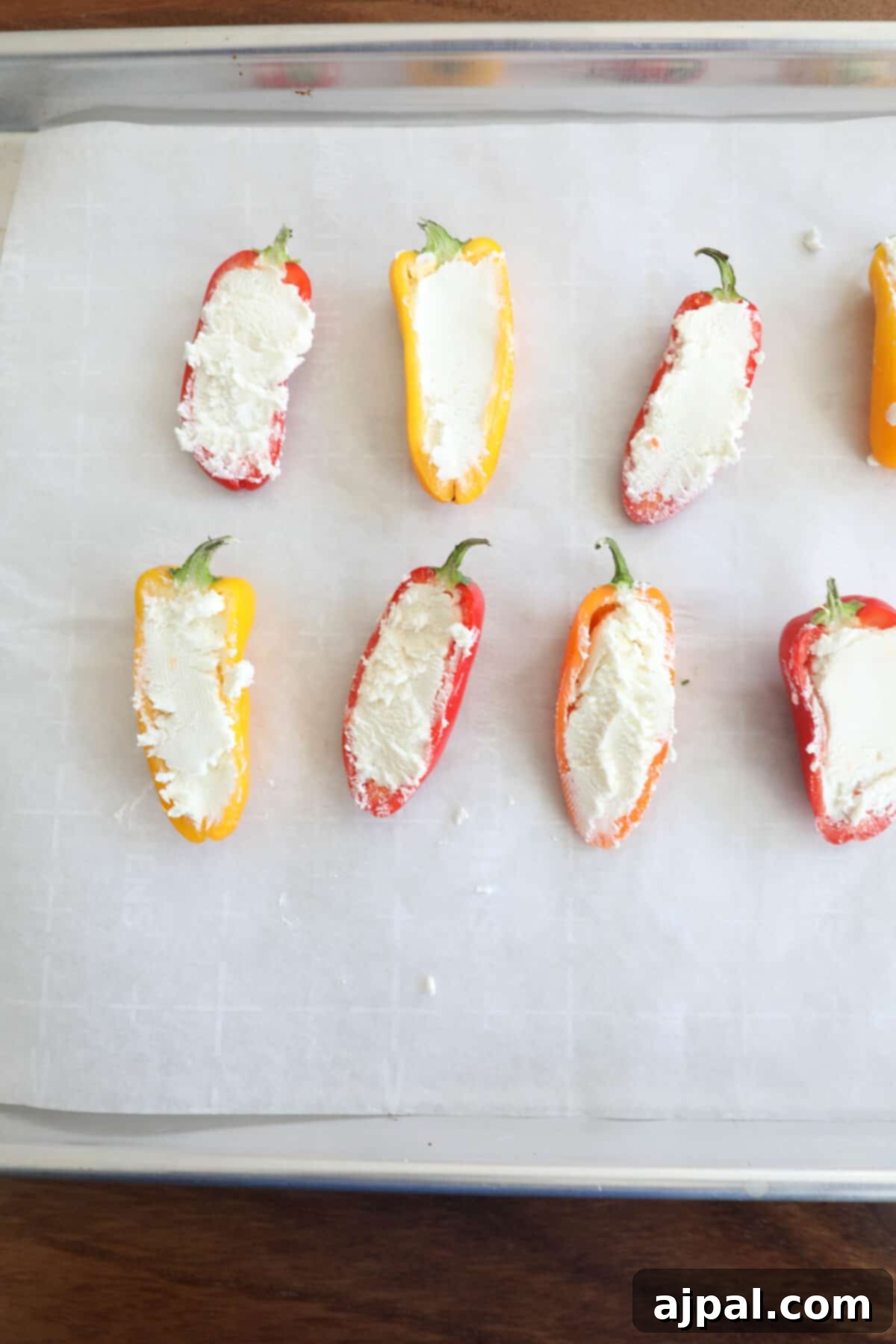 Goat Cheese Stuffed Peppers 7 Mini bell peppers meticulously stuffed with a generous amount of creamy goat cheese, arranged on a baking sheet, ready for baking.