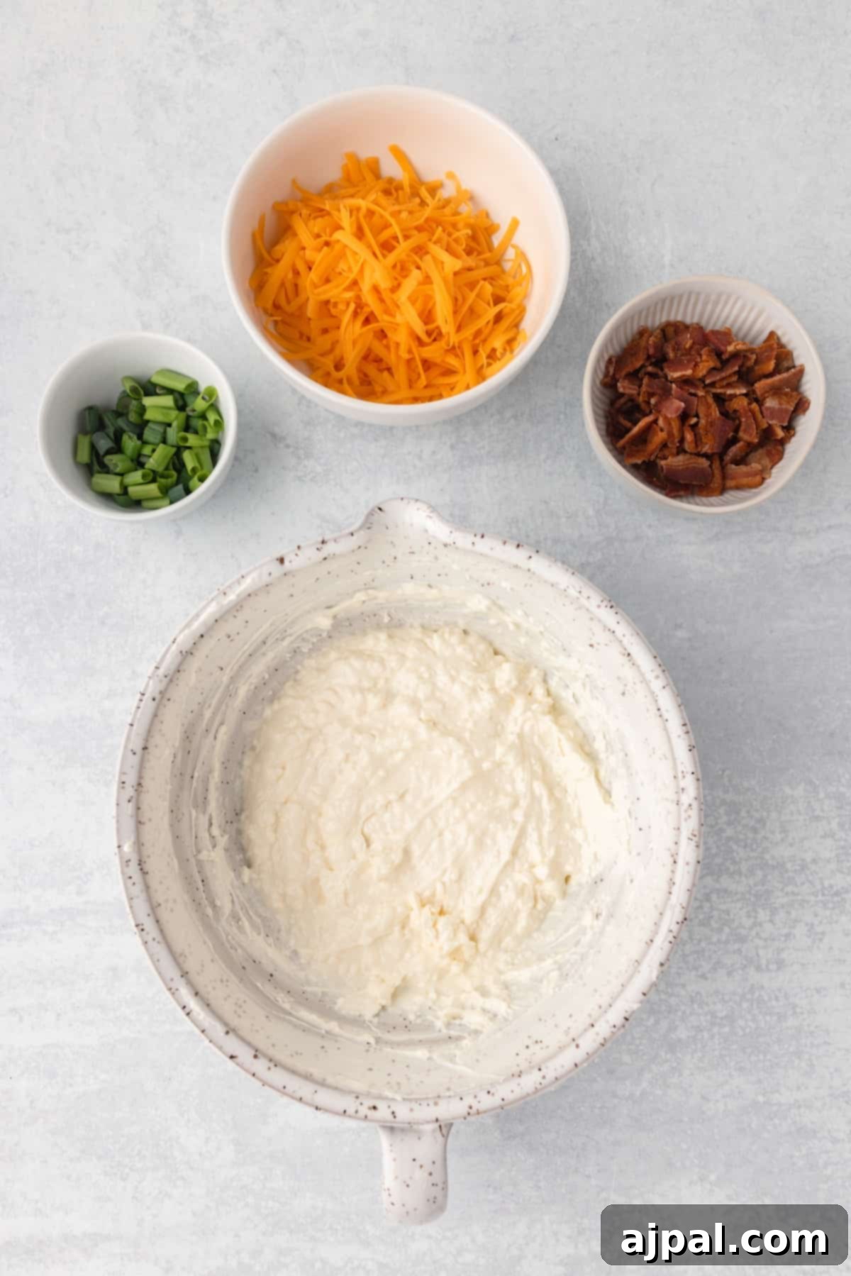 Grand Occasion Dip 6 Various ingredients for a cheesy mashed potatoes recipe, including cheese, herbs, and potatoes, are arranged on a surface.
