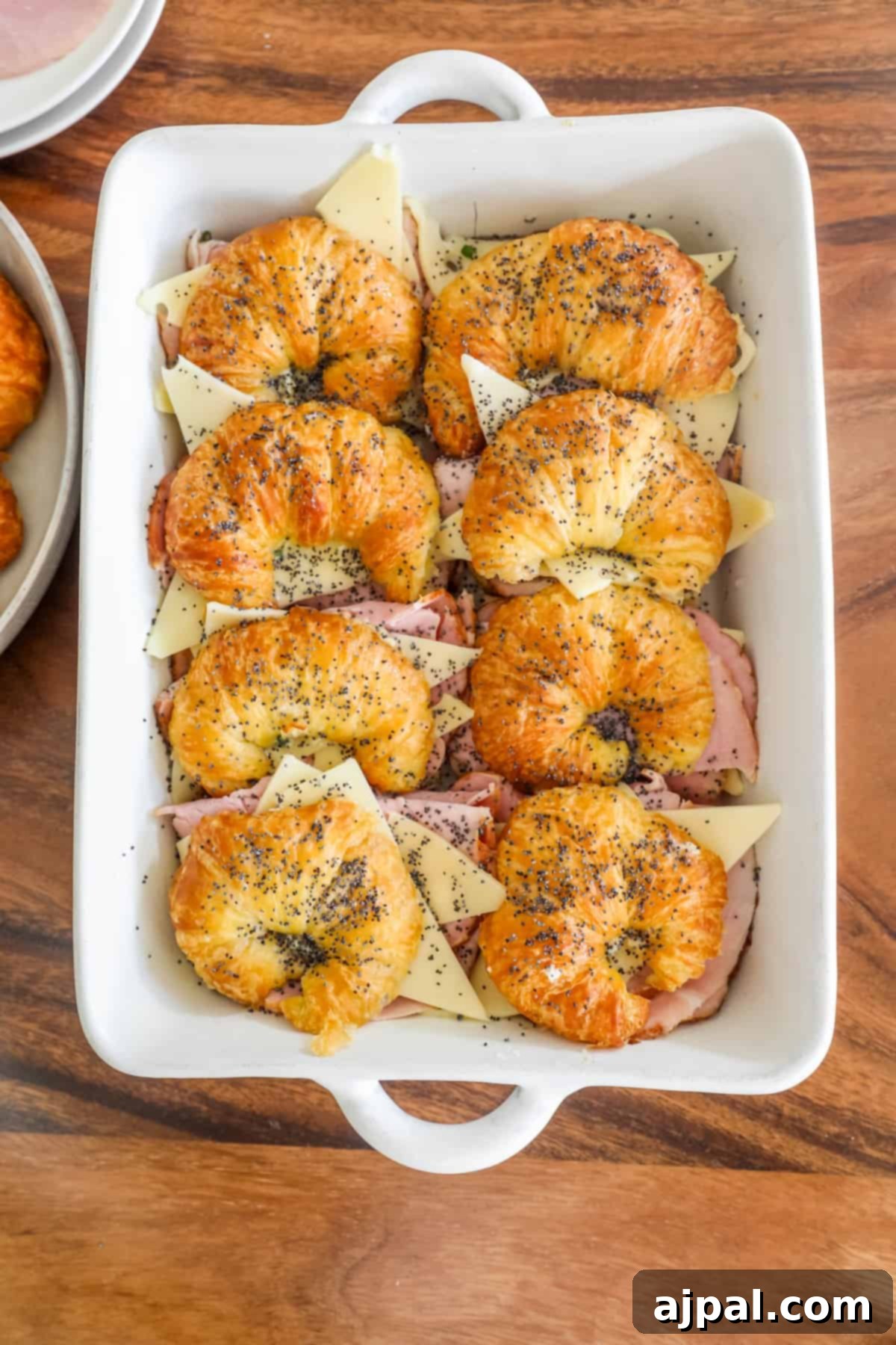 Warm Ham and Cheese Croissant Melts 13 Ham and cheese croissants arranged in a white baking dish, ready for baking.