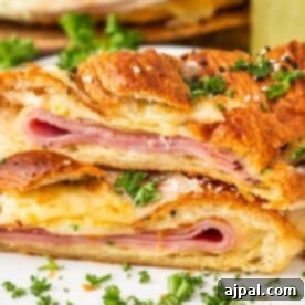 Two slices of braided puff pastry filled with ham and melted cheese, reminiscent of baked ham and cheese croissants, garnished with chopped parsley and sesame seeds, served on a white plate.