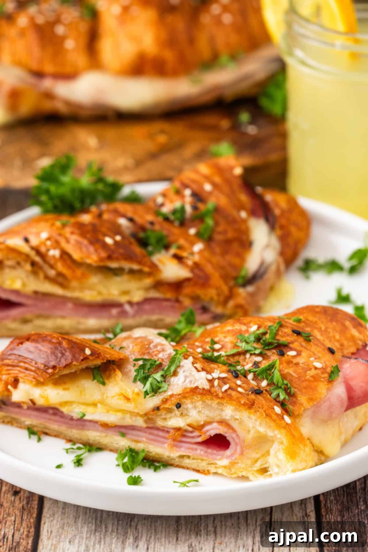 Warm Ham and Cheese Croissant Melts 5 Baked ham and cheese croissant cut in half, garnished with sesame seeds and parsley, served with lemonade.