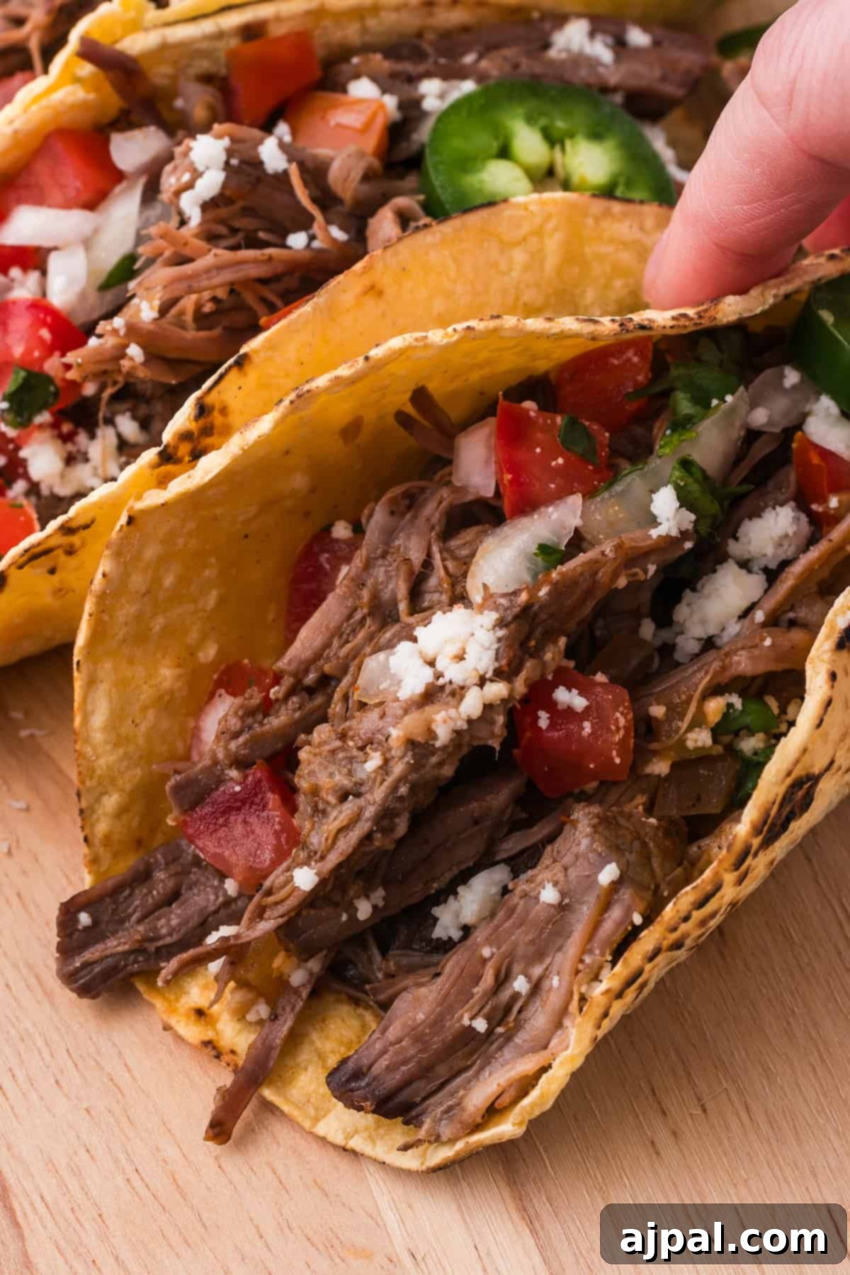 Tender Braised Beef Tacos 11 A hand holding a shredded beef taco filled with shredded beef, cheese, and vegetables.