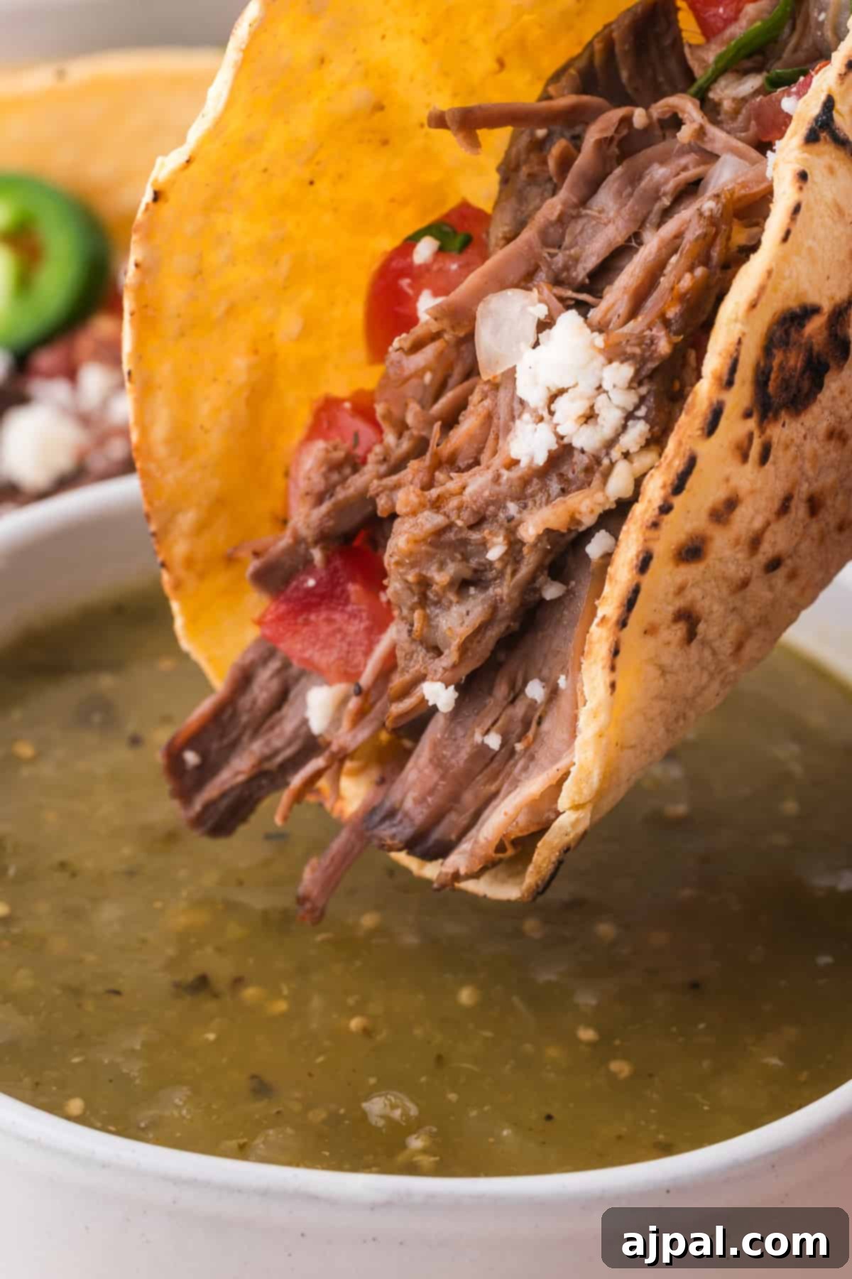 Tender Braised Beef Tacos 12 Beef Tacos with shredded beef and toppings, partially dipped in a bowl of broth.