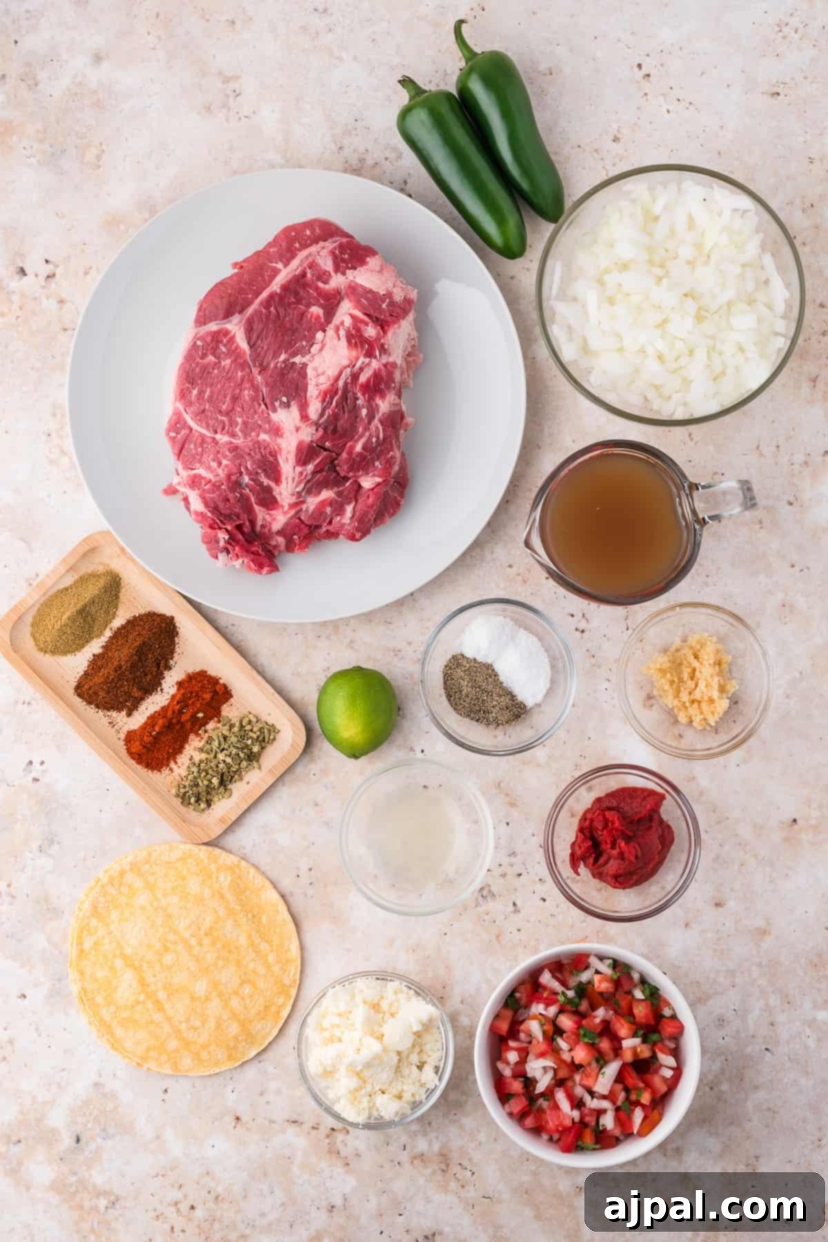 Tender Braised Beef Tacos 5 Ingredients for Shredded Beef Tacos arranged on a countertop, featuring steak, jalapeños, onions, spices, lime, broth, cheese, and salsa.
