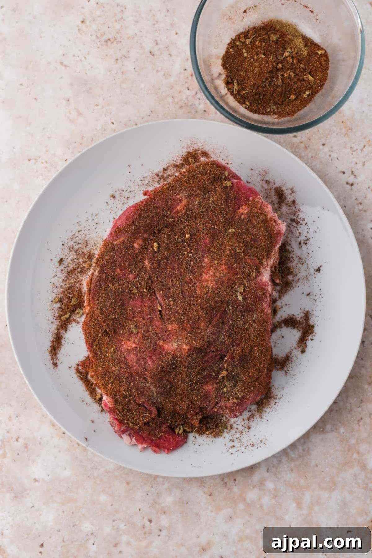 Tender Braised Beef Tacos 6 A raw beef chuck roast seasoned generously with a dry spice rub, resting on a clean white plate, perfectly prepared for the slow cooking process.