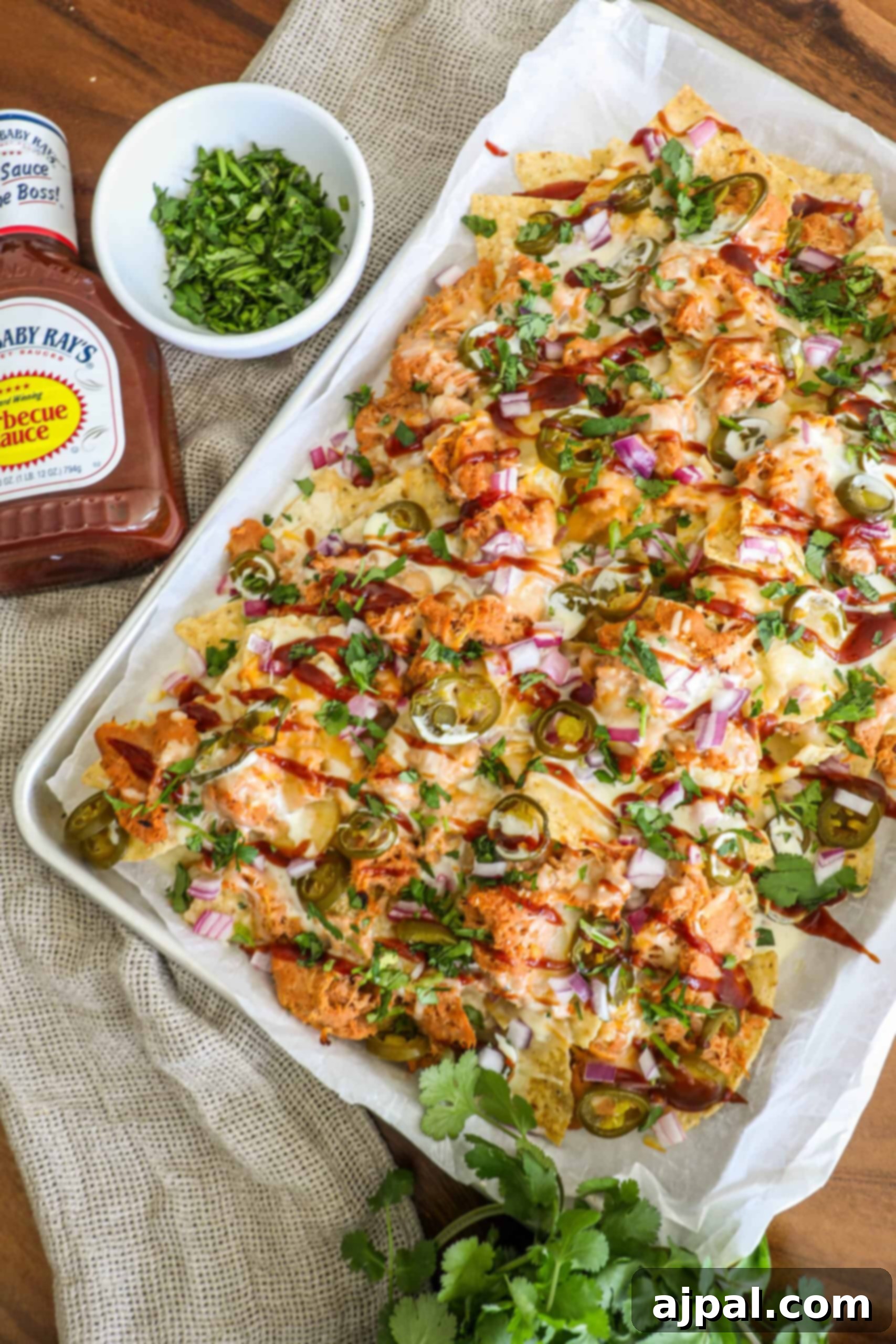 A vibrant platter of BBQ chicken nachos, generously loaded with melted cheese, succulent shredded chicken, sharp red onions, bright green jalapeños, and fresh cilantro, promising a delightful culinary experience.
