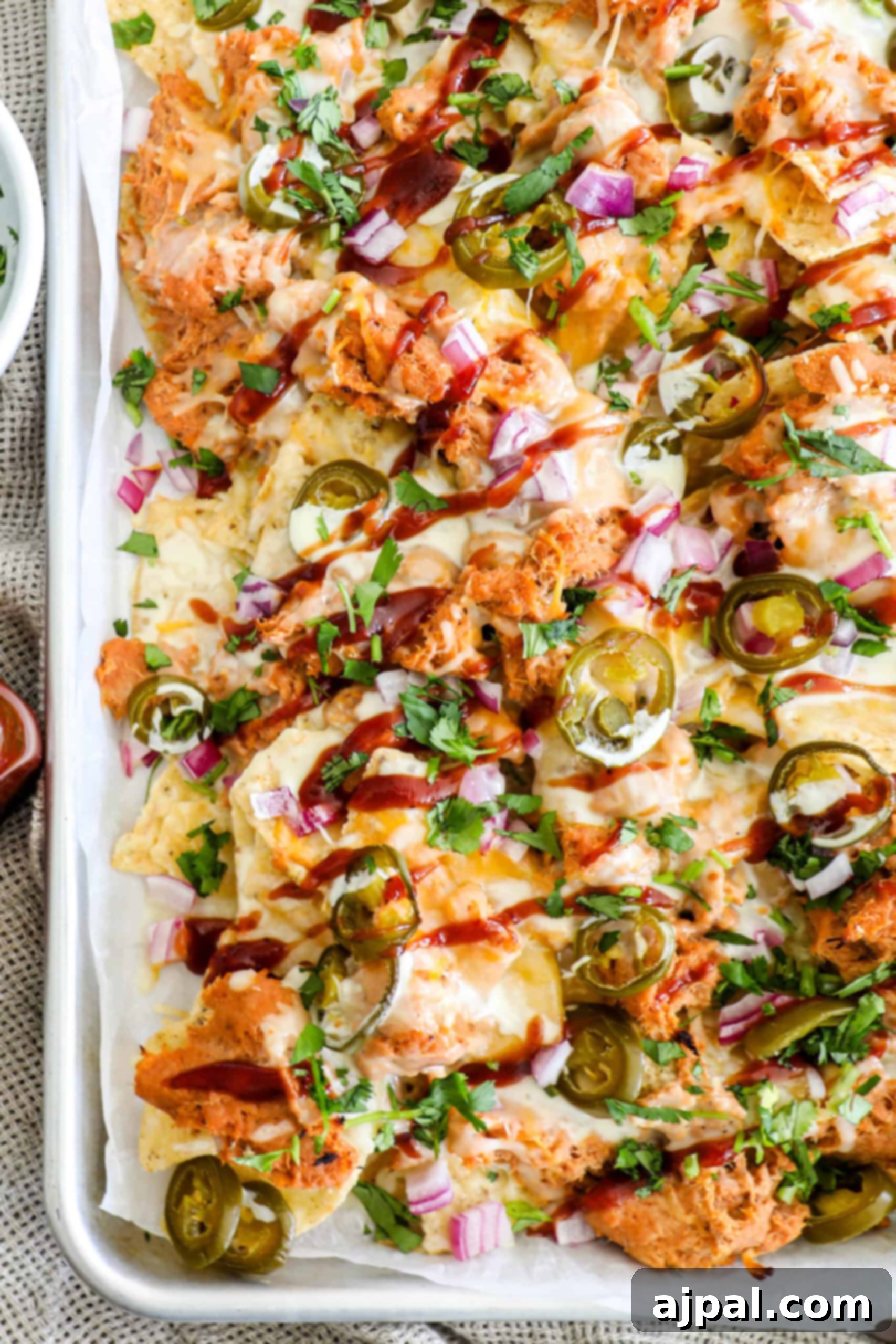 A large tray of BBQ chicken nachos, richly topped with melted cheese, tender shredded chicken, bright jalapeños, crisp red onions, and fresh cilantro, promising a delicious and satisfying meal.