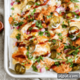 A tray of bbq chicken nachos topped with melted cheese, jalapeños, diced red onions, and fresh cilantro, drizzled with barbecue sauce.