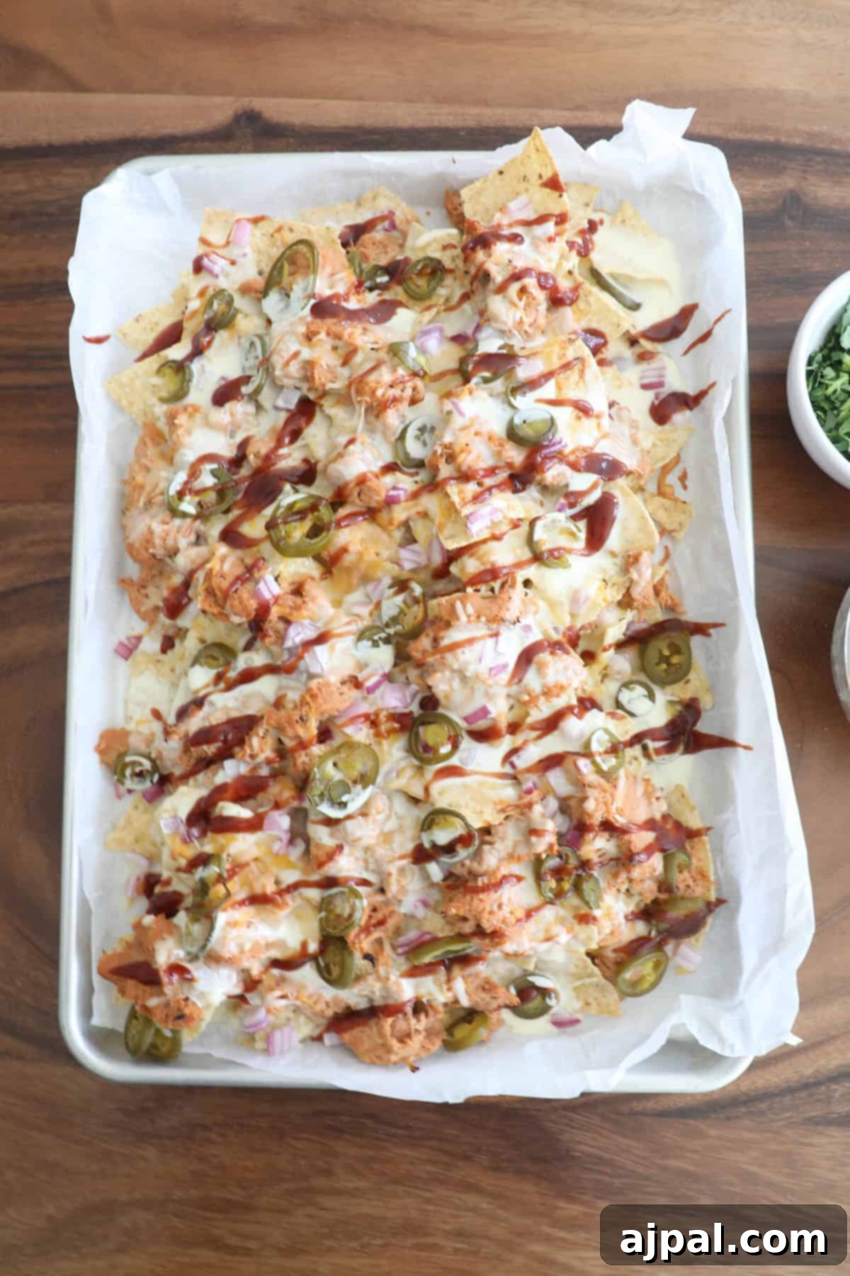 A tray of nachos topped with cheese, chicken, jalapeños, and a drizzle of sauce, served on a wooden table.