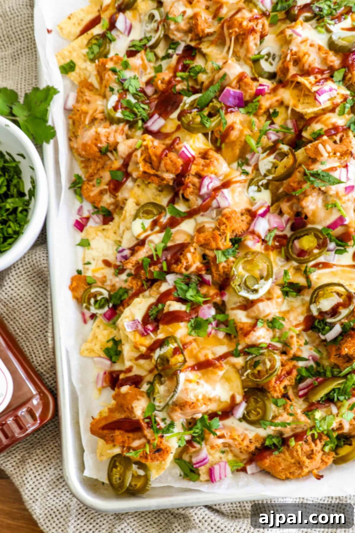 A generously loaded tray of BBQ chicken nachos, featuring tender shredded chicken, zesty jalapeños, crisp red onions, perfectly melted cheese, and a vibrant garnish of fresh cilantro.