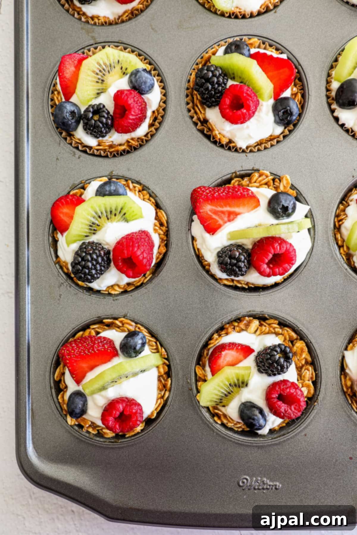 Fruity Granola Bites 2 Granola in a muffin holder with creamy yogurt and a colourful array of fresh fruit, including strawberries, blueberries, raspberries, and kiwi slices.