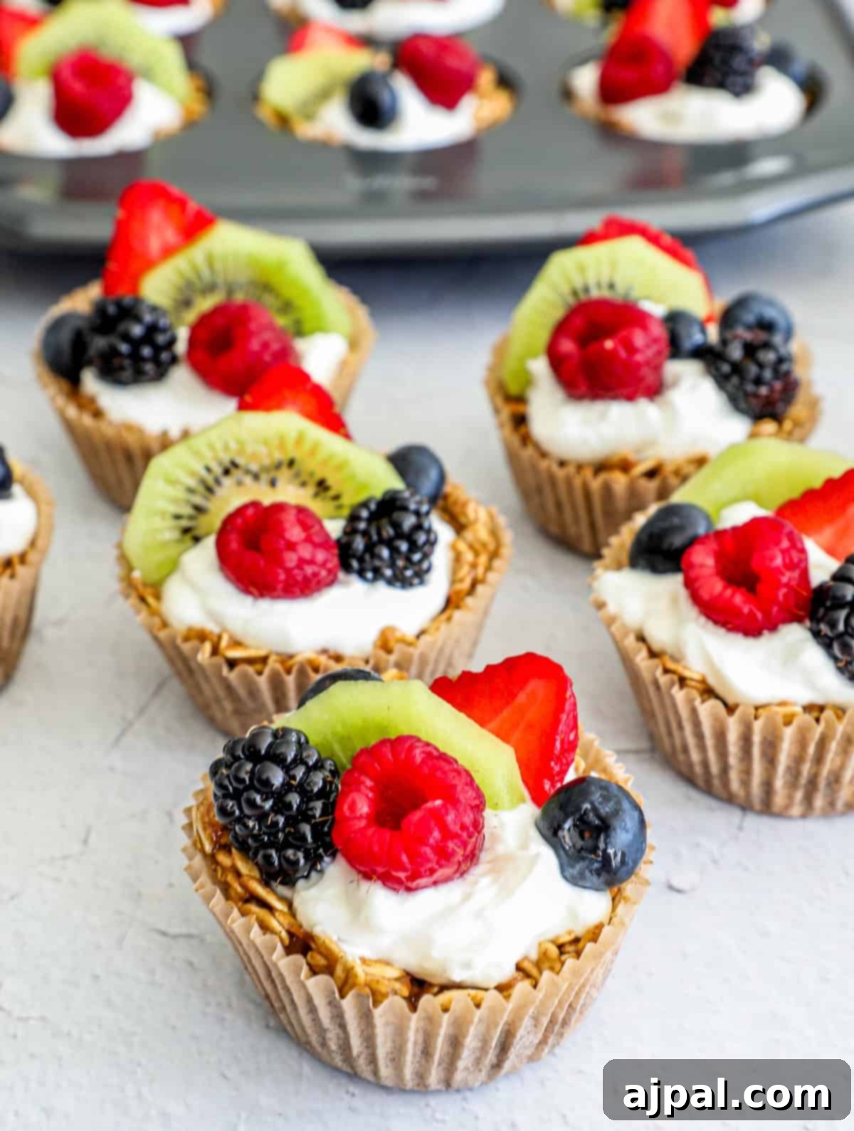 Fruity Granola Bites 4 A close-up of a granola fruit cup in a muffin liner, showcasing the layered base, yogurt, and mixed fresh fruit toppings, including strawberries, blueberries, and kiwi.