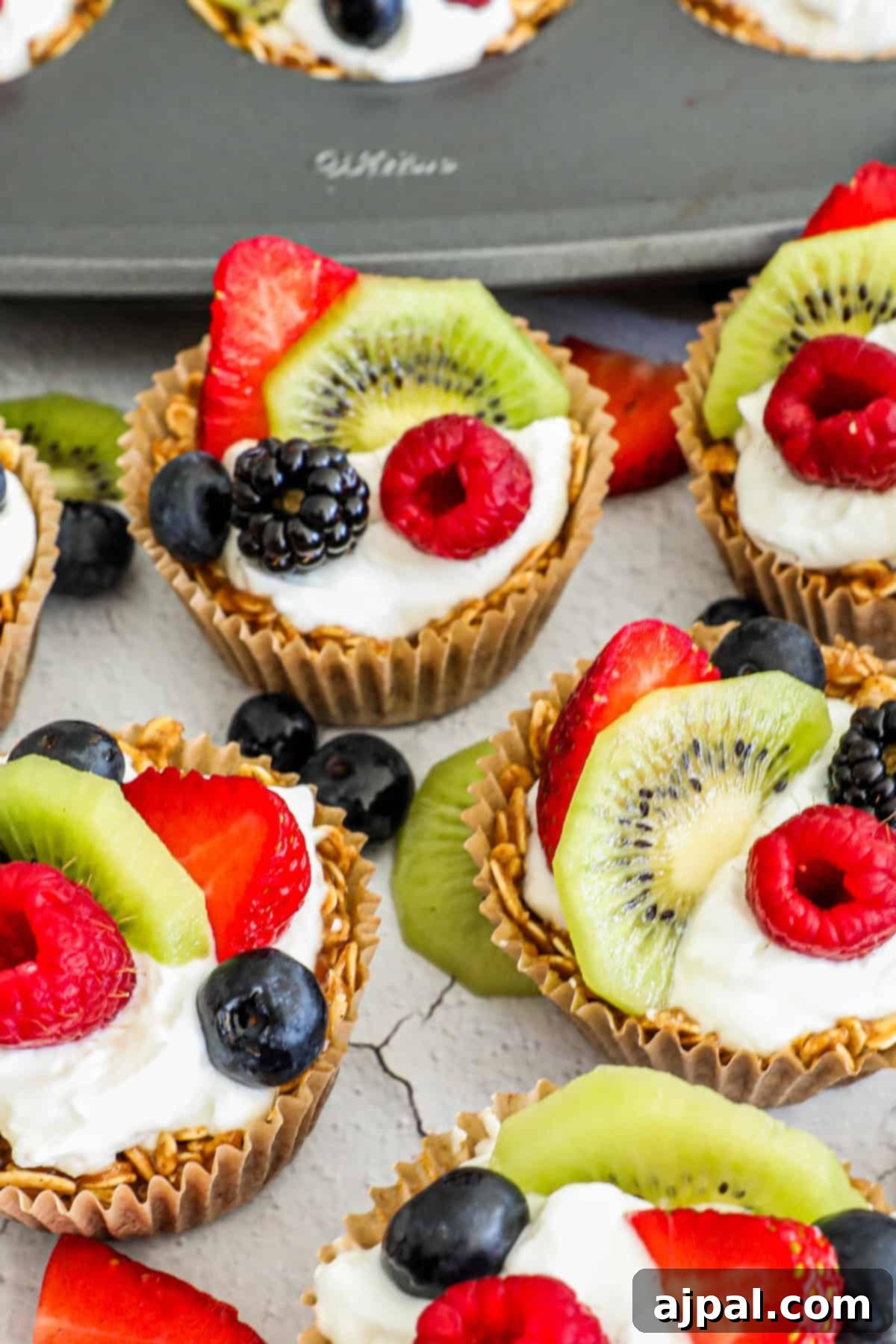 Fruity Granola Bites 5 A top-down view of two granola fruit cups, meticulously arranged in a muffin tin with vibrant fresh fruits and creamy yogurt.