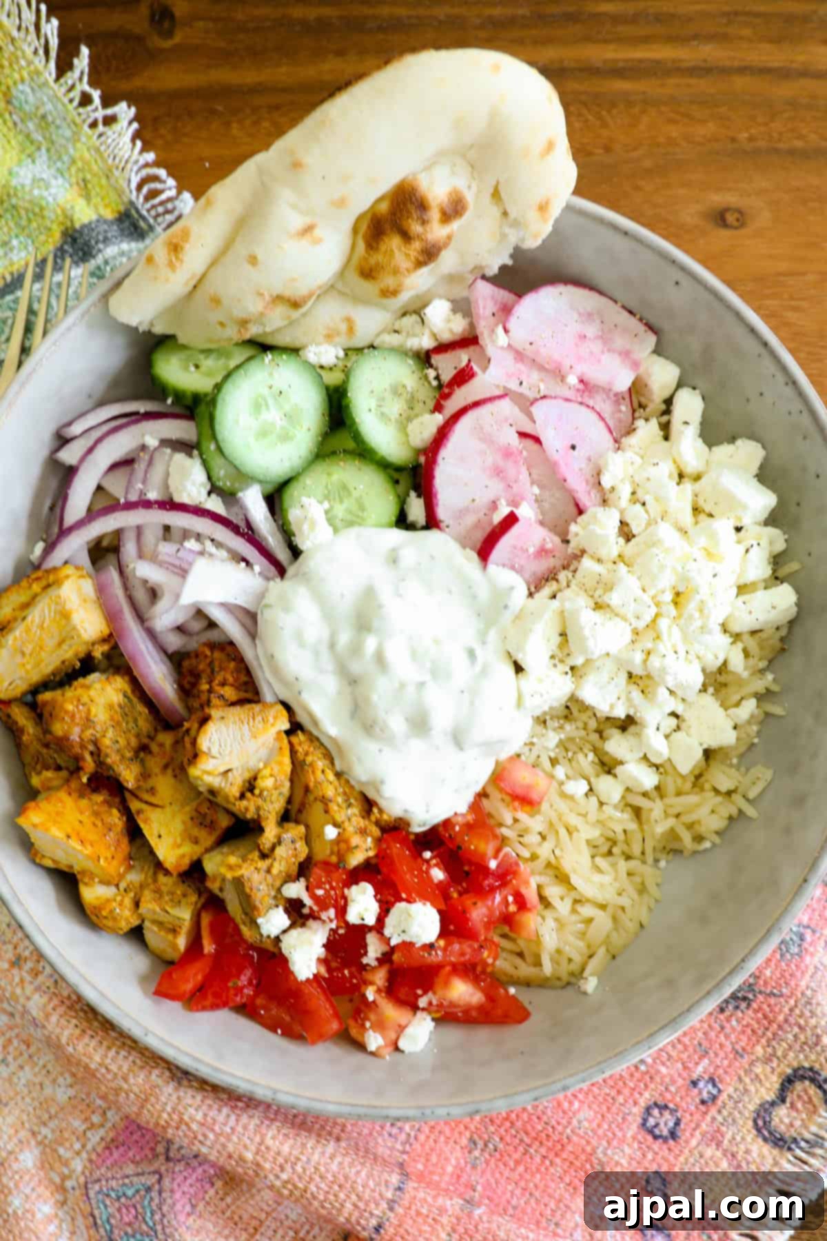 A vibrant Greek Chicken Bowl featuring tender chicken, fresh vegetables, and creamy tzatziki over a bed of rice.