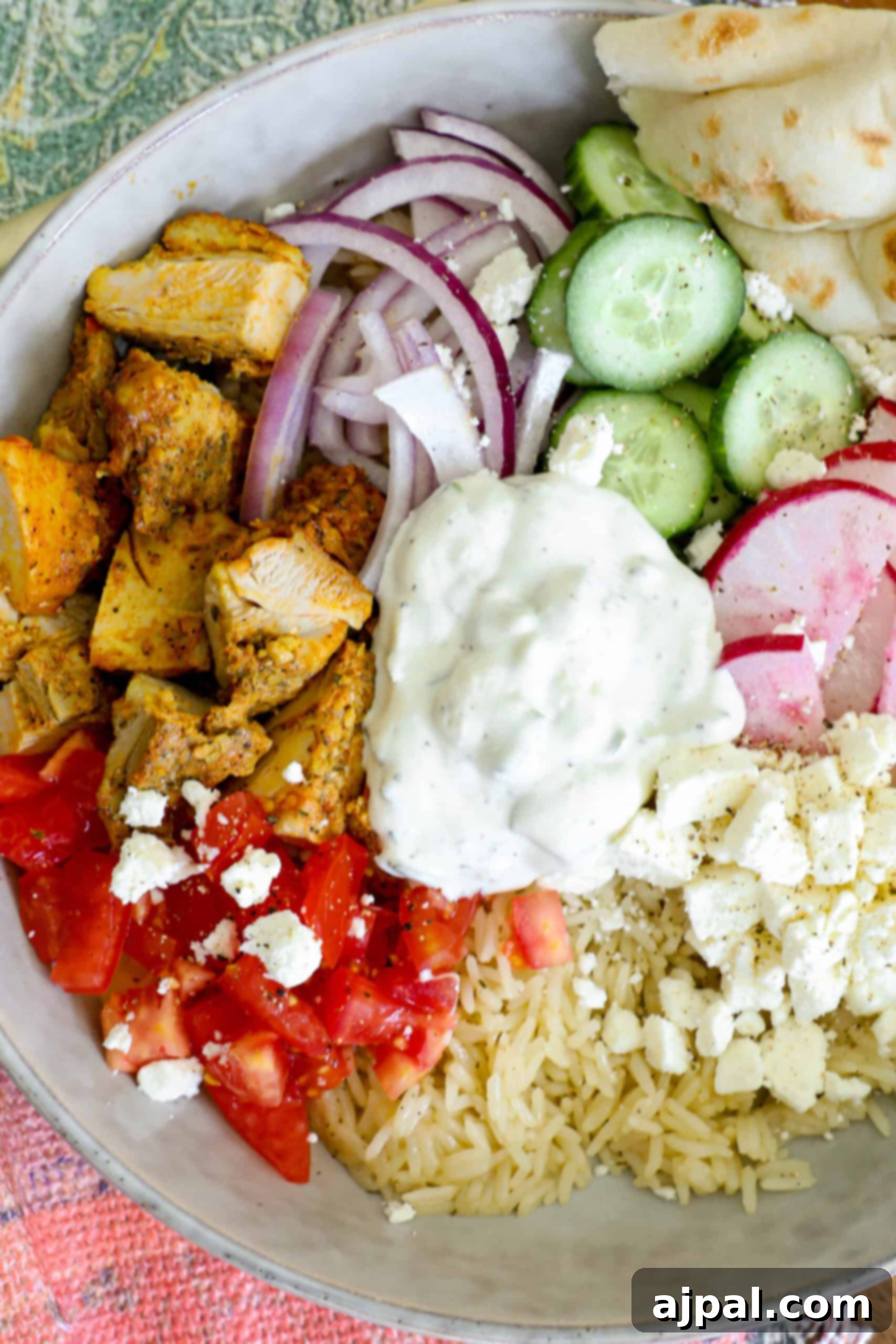 A complete Greek Chicken Bowl, served with warm pita bread on the side, showcasing all the delicious toppings.