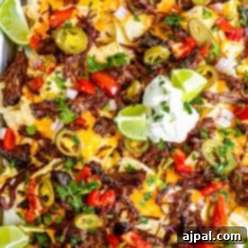 Platter of loaded carne asada nachos topped with jalapeños, tomatoes, cheese, and sour cream.