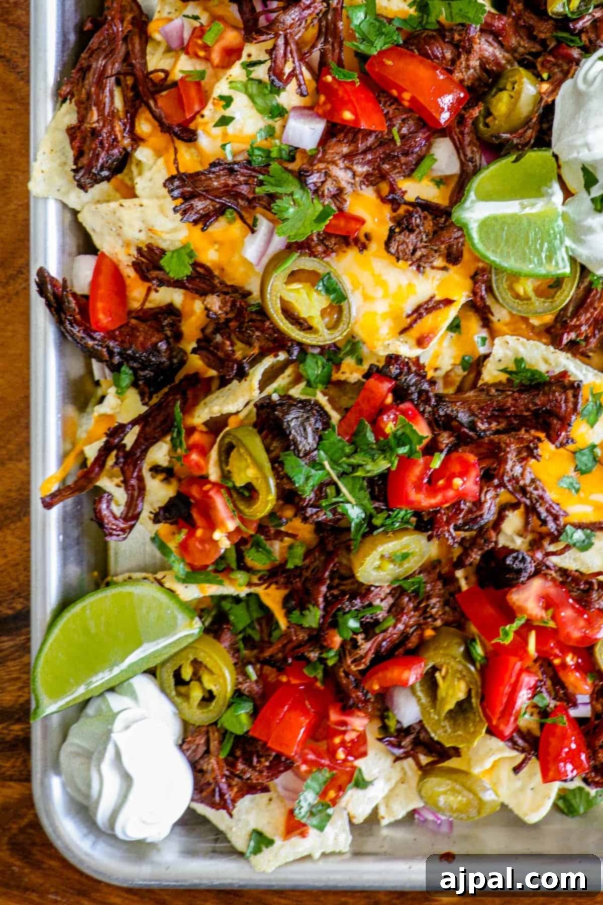 Loaded Carne Asada Nachos 3 Close-up shot of a tray of cheesy carne asada nachos, showing the layers of tender meat, melted cheese, chives, and jalapenos.