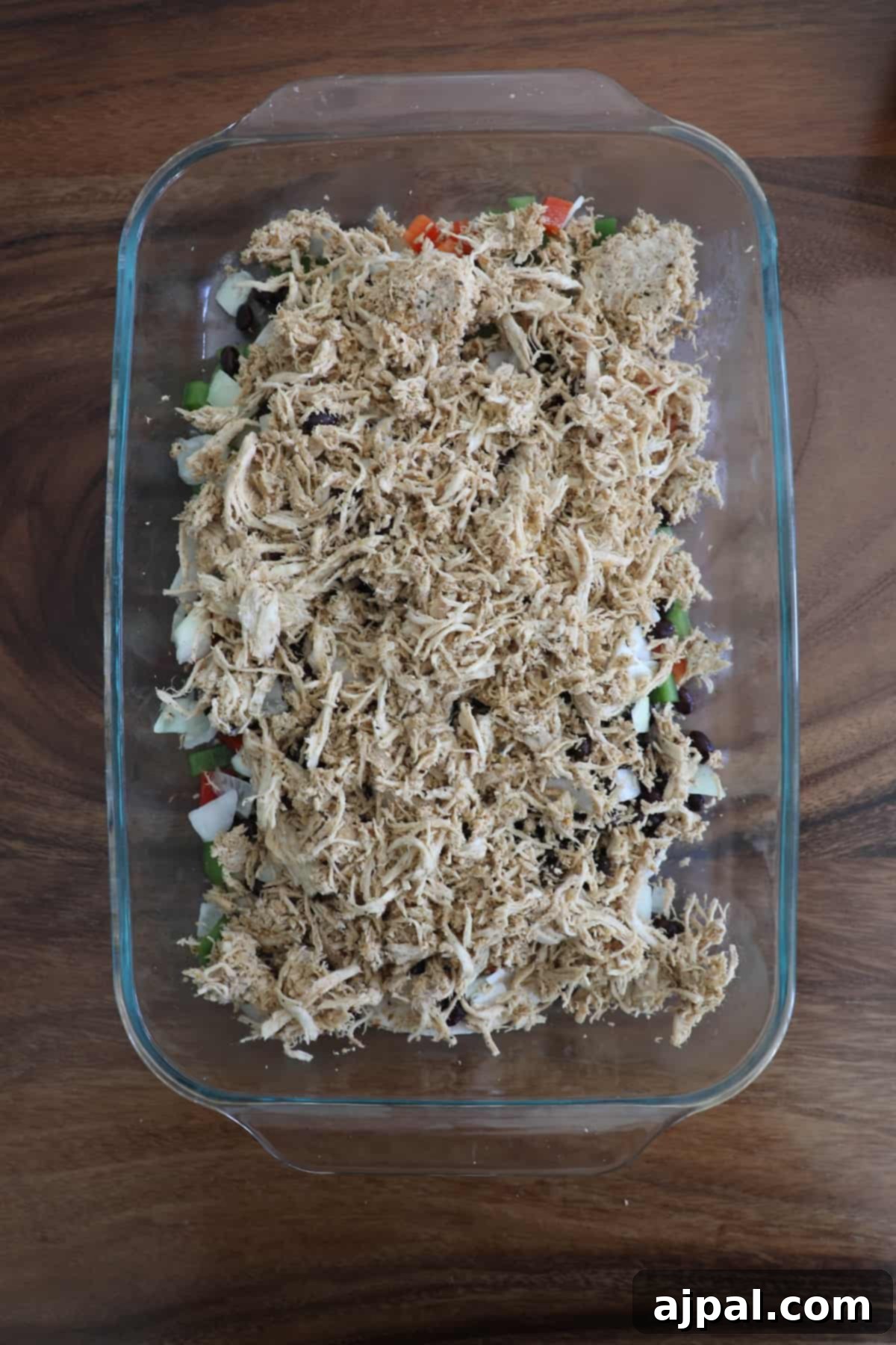 Half of the seasoned chicken, black beans, onions, bell peppers, and jalapeno layered over tortillas in a baking dish.