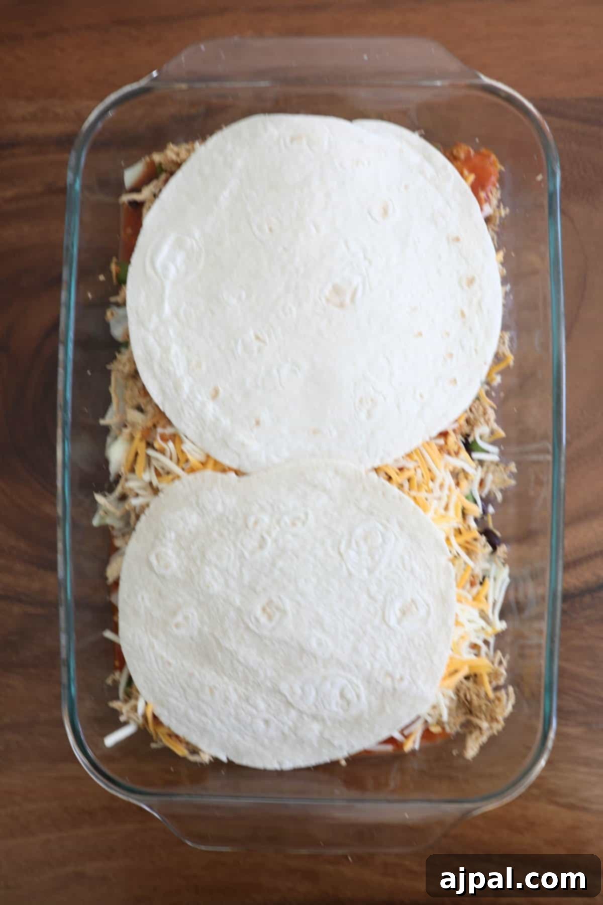 The second layer of tortillas, chicken, vegetables, sauce, and cheese being assembled in the baking dish.
