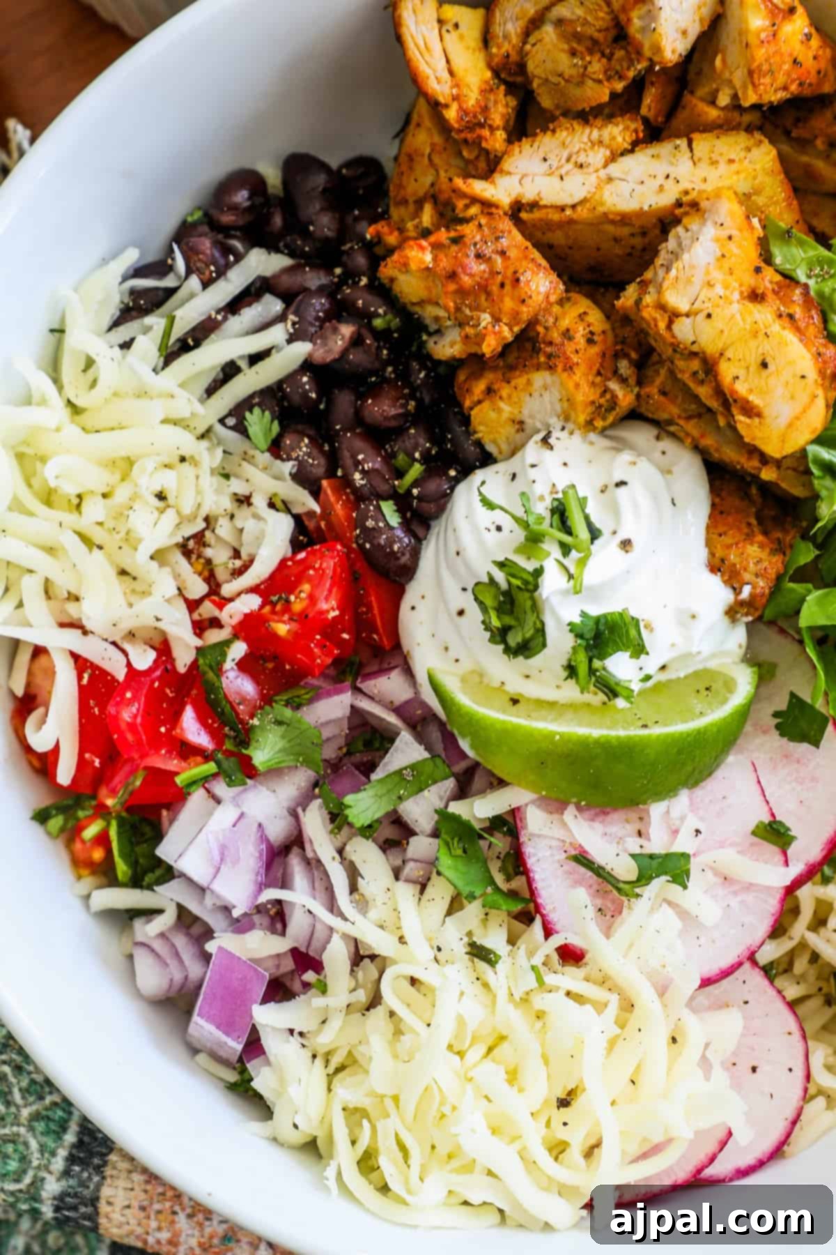 Flavorful Chicken Burrito Bowls 7 chicken, lettuce, black beans, tomatoes, lime, and sour cream in a bowl with radishes and cheese