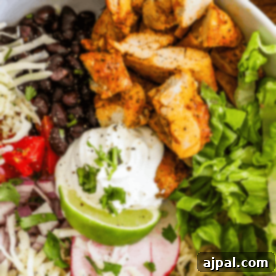 Flavorful Chicken Burrito Bowls 9 A bowl containing grilled chicken pieces, black beans, shredded cheese, chopped tomatoes, sour cream, lettuce, lime, radish slices, and diced onions, garnished with cilantro—perfect for hearty chicken burrito bowls.