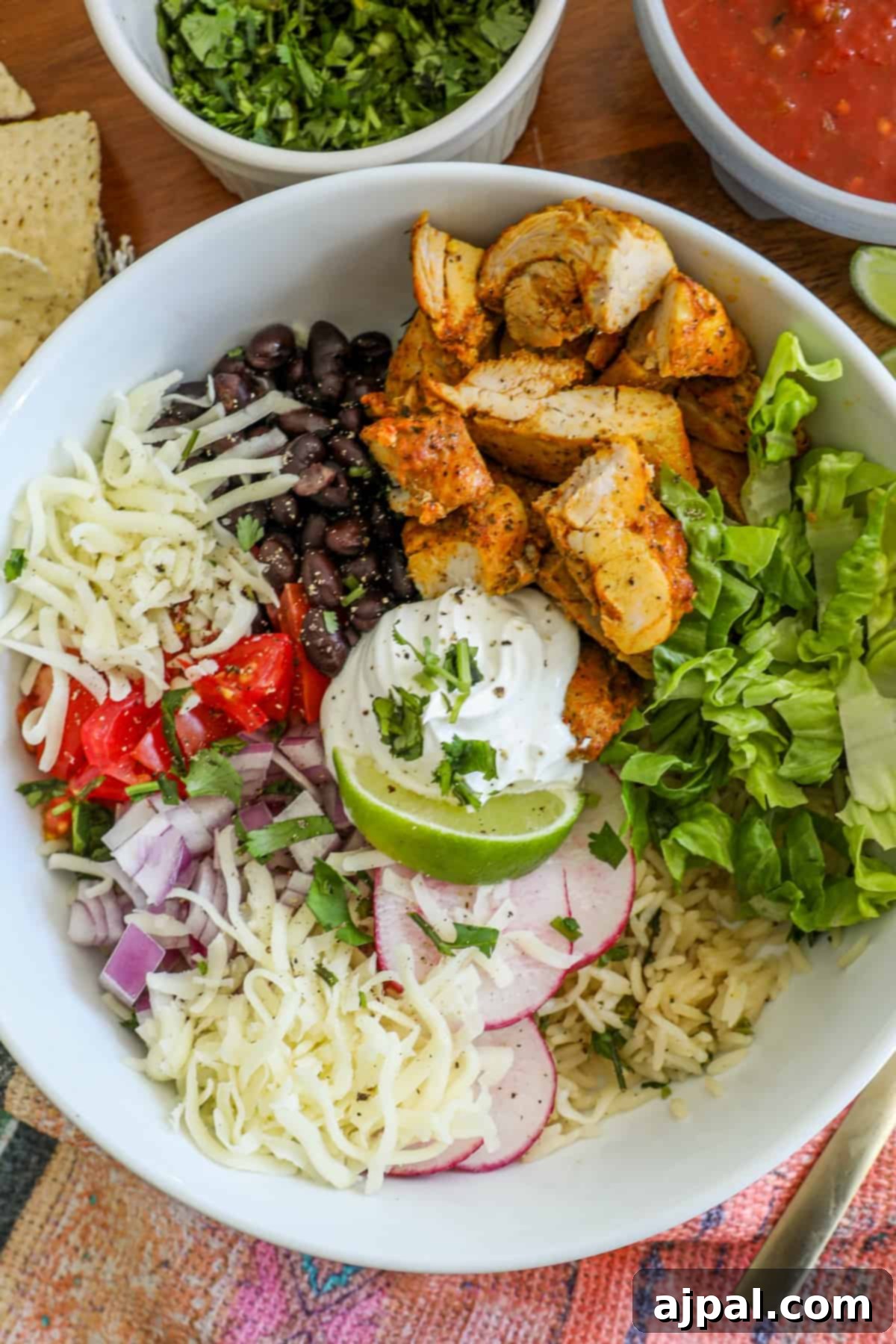 Flavorful Chicken Burrito Bowls 3 chicken, lettuce, black beans, tomatoes, lime, and sour cream in a bowl with radishes and cheese