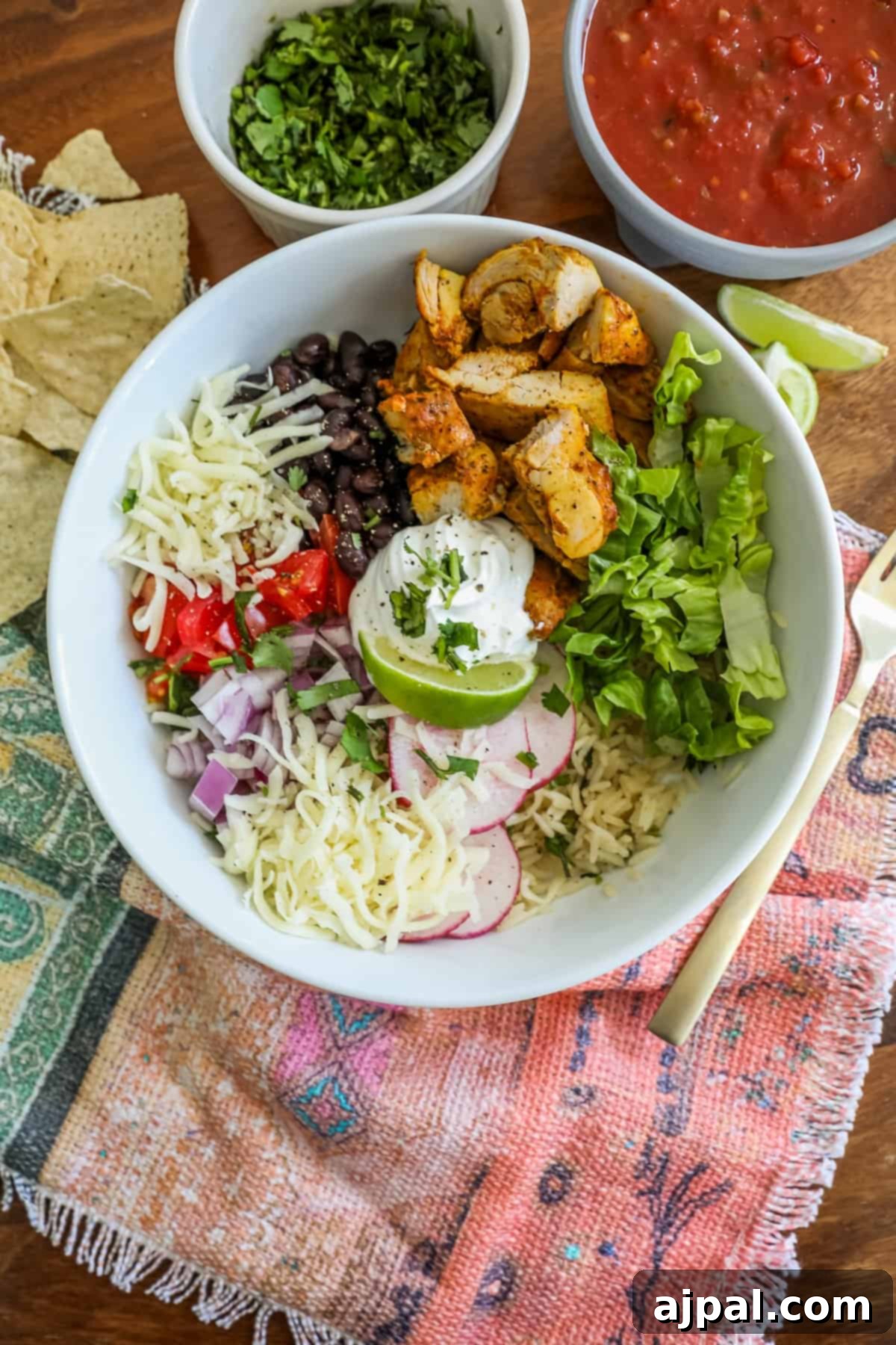 Flavorful Chicken Burrito Bowls 4 chicken, lettuce, black beans, tomatoes, lime, and sour cream in a bowl with radishes and cheese