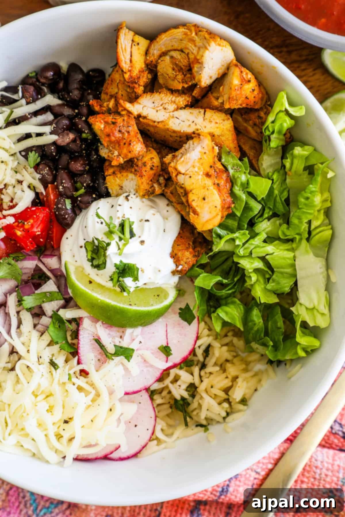 Flavorful Chicken Burrito Bowls 5 chicken, lettuce, black beans, tomatoes, lime, and sour cream in a bowl with radishes and cheese