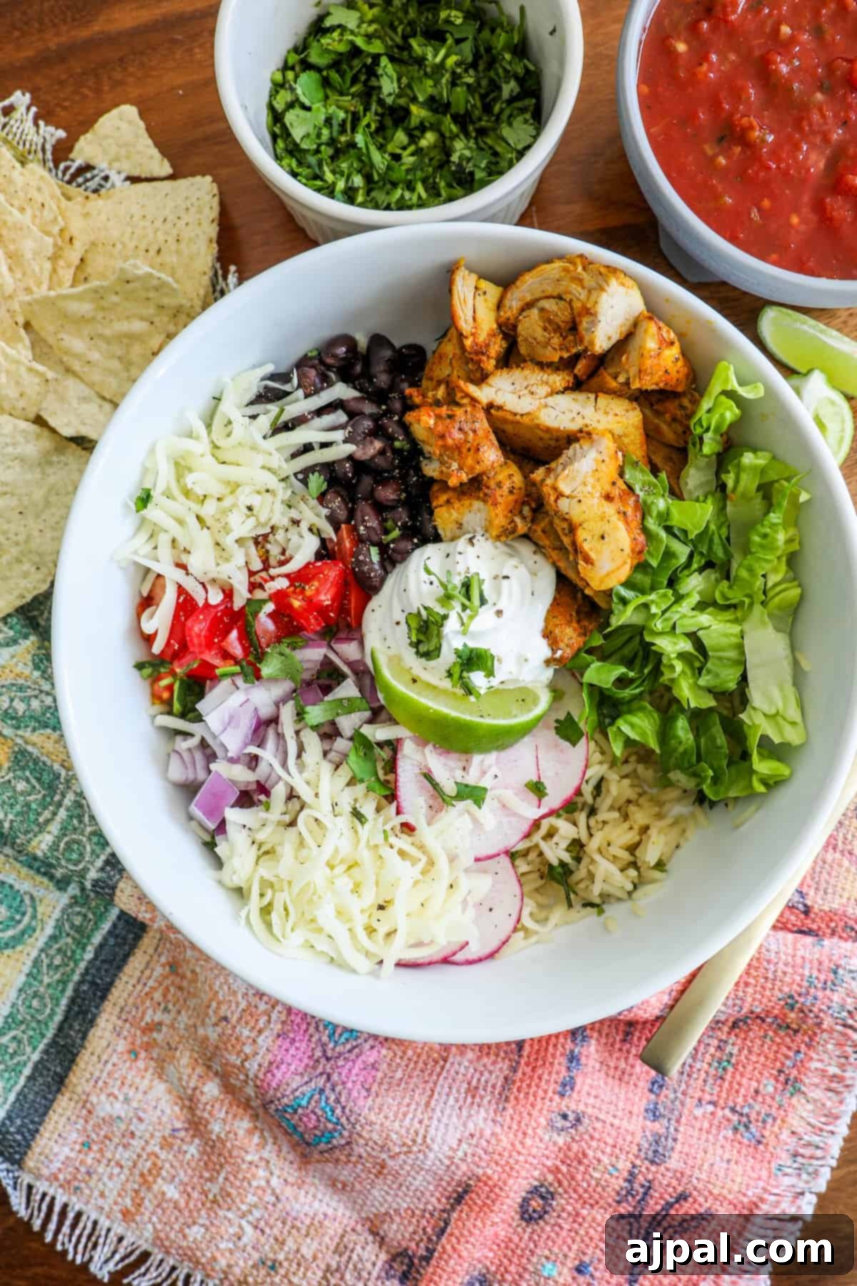 Flavorful Chicken Burrito Bowls 6 chicken, lettuce, black beans, tomatoes, lime, and sour cream in a bowl with radishes and cheese