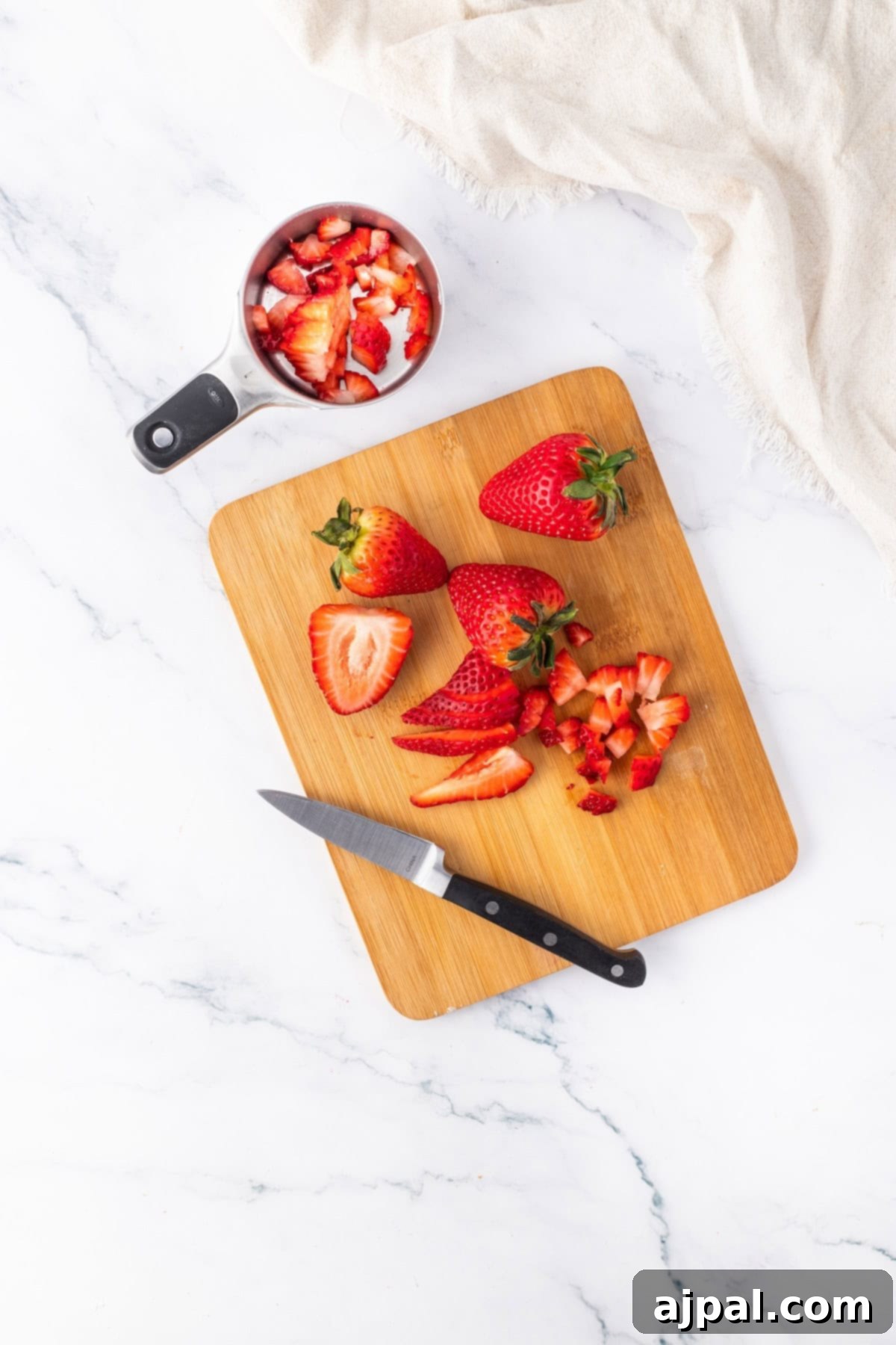 Fresh strawberries arranged on a wooden board, with some in a measuring cup, showcasing the main ingredient.