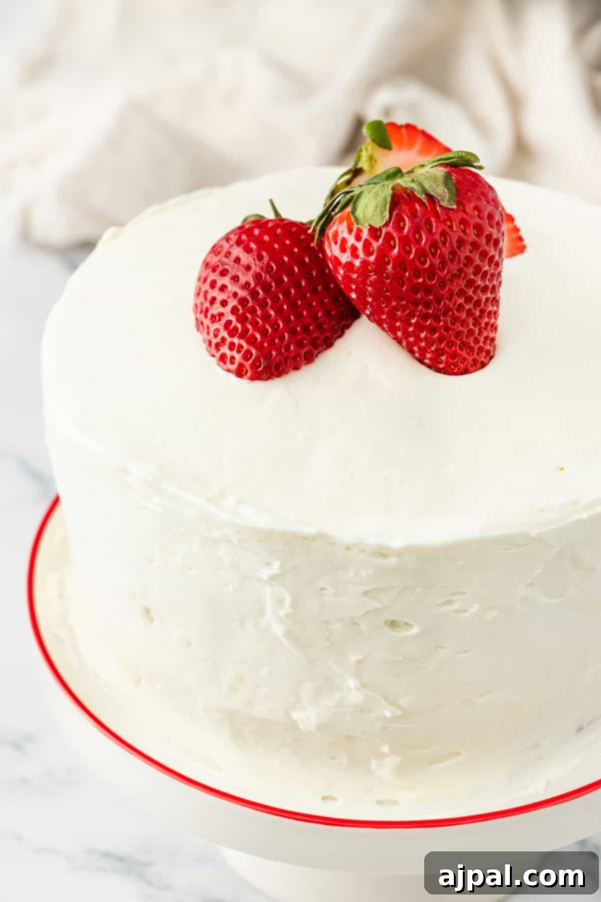 White frosted cake decorated with whole fresh strawberries on top and around the sides.