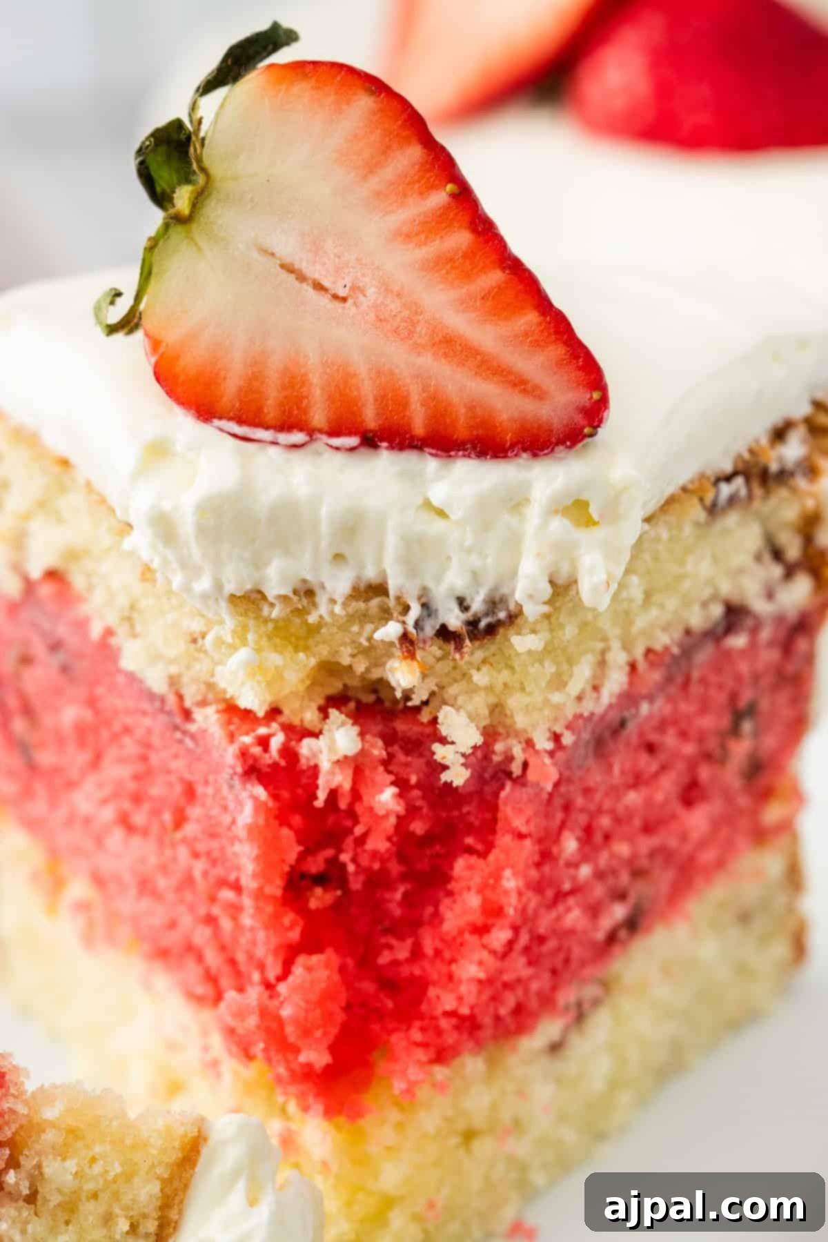 Two-layer vanilla cake with one strawberry layer, frosted in white cream and topped with a halved fresh strawberry.