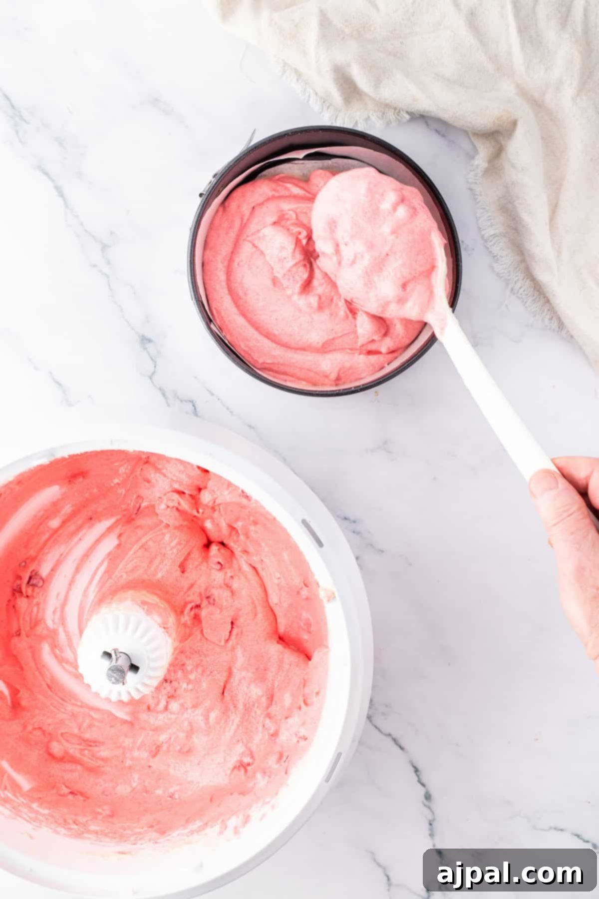 Pink cake batter being poured into a round cake pan, ready for baking.