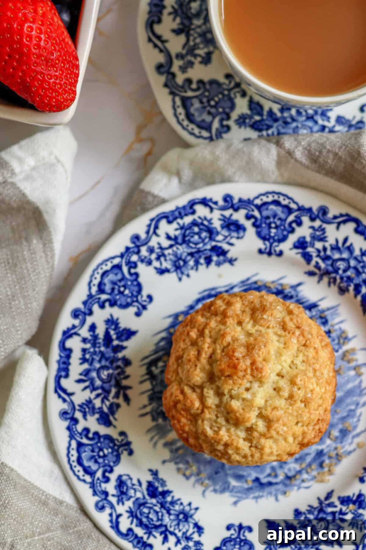 A freshly baked scone on a blue and white patterned plate with a cup of tea and strawberries in the background.