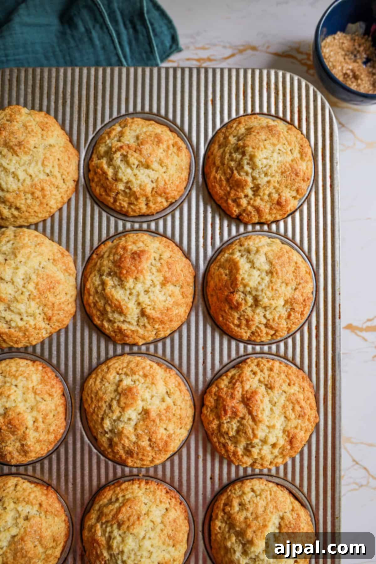 A dozen freshly baked muffins cooling on a striped cloth, displayed in a symmetric arrangement on a metal tray.