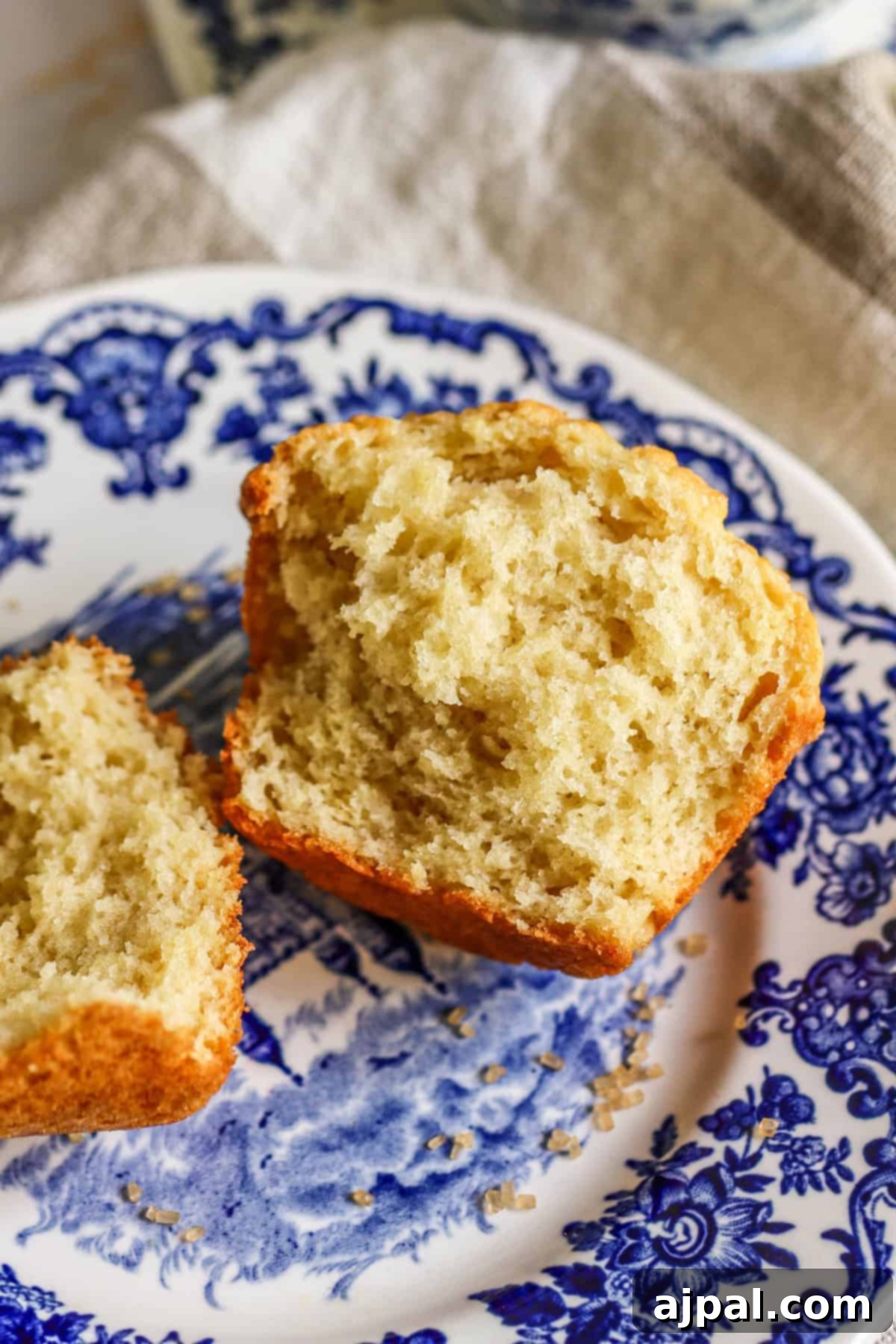 Close-up of a freshly baked muffin split in half on a blue and white patterned plate, highlighting its fluffy texture.