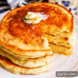 A stack of fluffy pancakes with butter and syrup on a plate, showing a bite taken out of the top pancake.