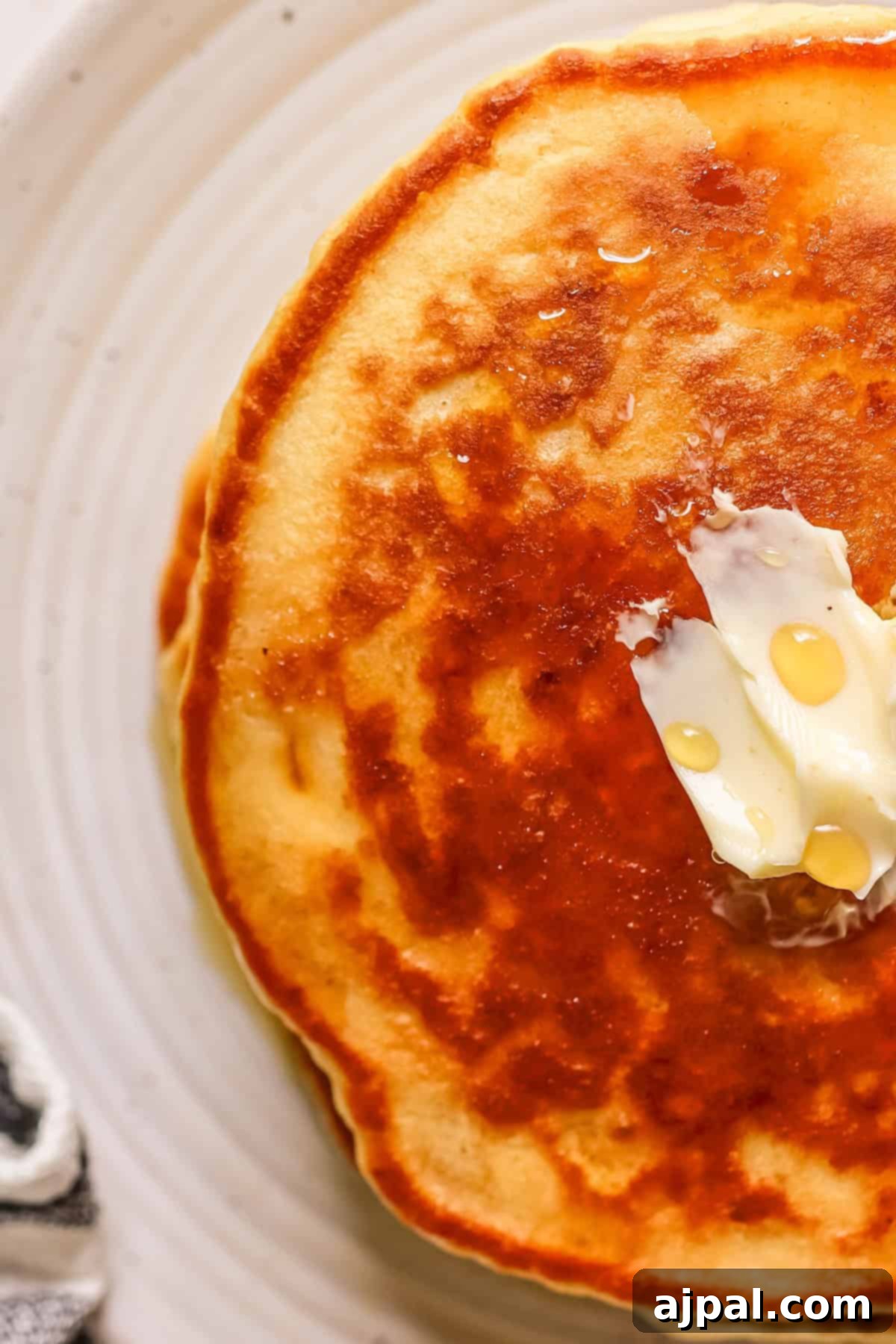 Tangy Sourdough Flapjacks 3 A single fluffy sourdough pancake with melting butter and a drizzle of maple syrup, served on a pristine white plate.