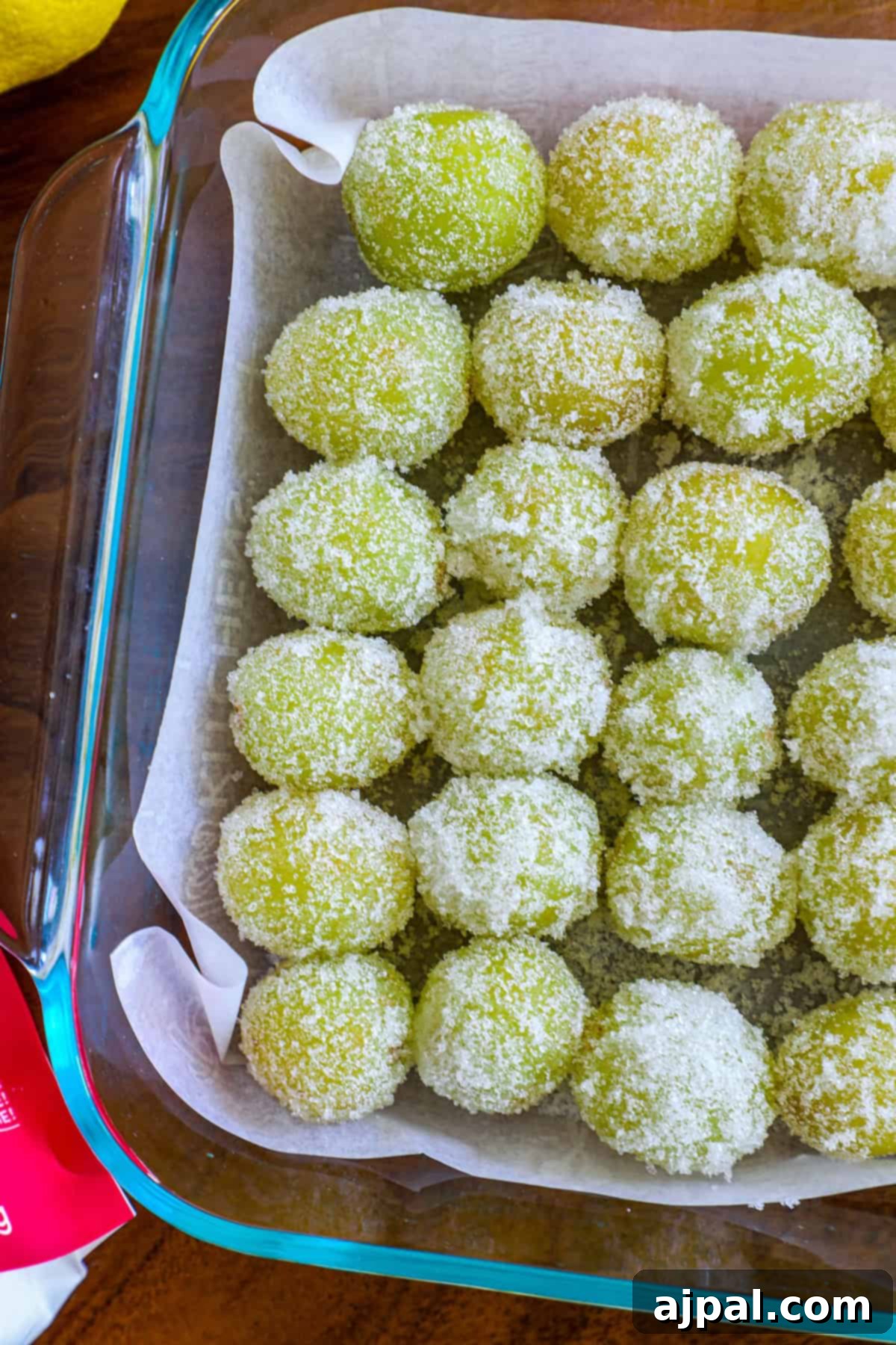 Zingy Sweet Grapes 9 A tray of green coconut-covered mochi balls arranged neatly on parchment paper in a baking dish.