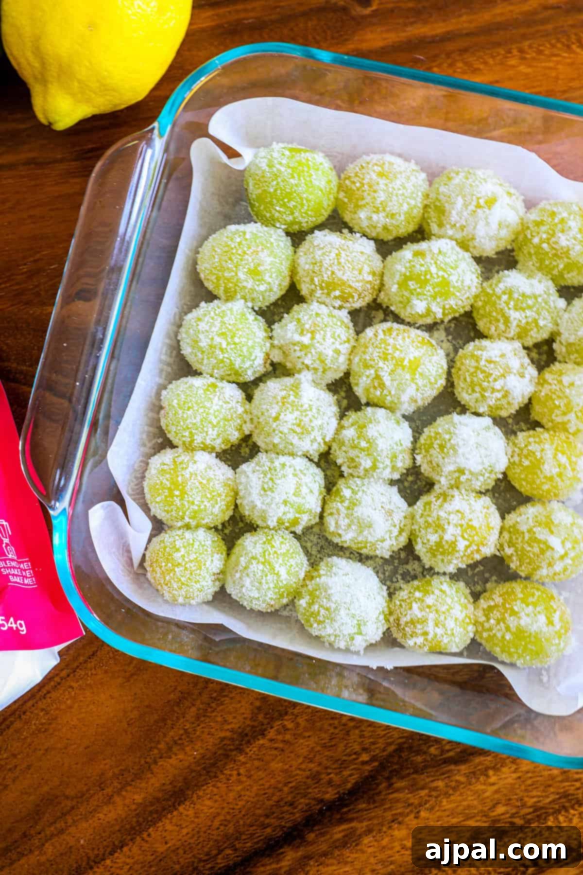 Zingy Sweet Grapes 3 A glass dish containing freshly made green coconut ladoos sprinkled with desiccated coconut, placed on a wooden table next to a lemon and a pink measuring spoon.