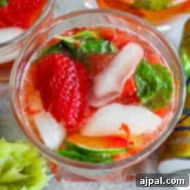 A close-up of a strawberry mojito drink with fresh strawberries, mint leaves, ice, and lime slices in a glass.