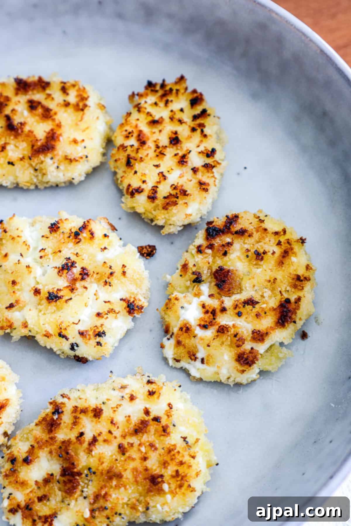 Golden-brown cauliflower steaks are served on a gray ceramic plate, exhibiting a crispy texture with subtly charred edges.
