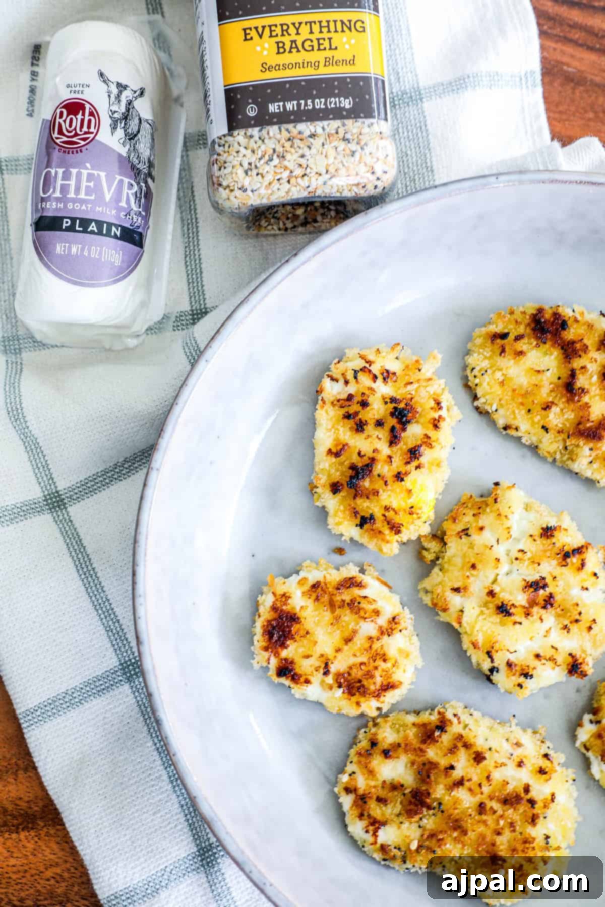 A plate featuring several goat cheese crusted chicken patties sits beside a block of Chevre goat cheese and a bottle of 'Everything Bagel' seasoning.
