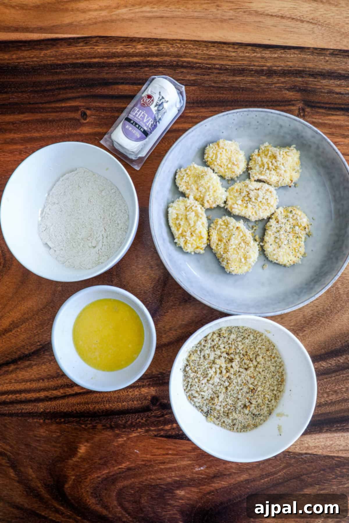 A close-up of recipe ingredients laid out on a wooden table, showing bowls of flour, melted butter, yogurt, and crushed cookies, ready for use.
