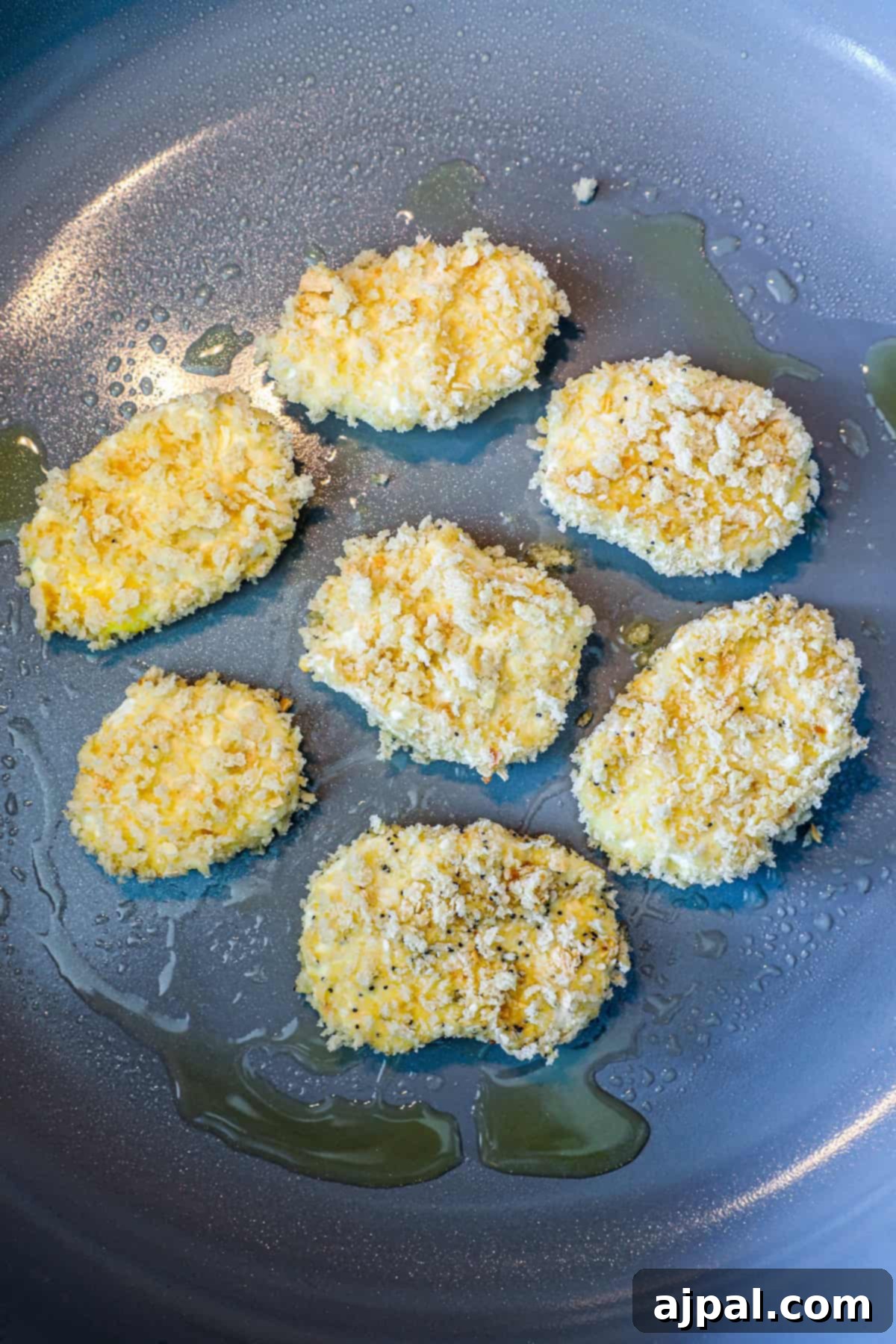 Several breaded chicken pieces are seen sizzling in hot oil within a vibrant blue skillet, creating a golden-brown crust.