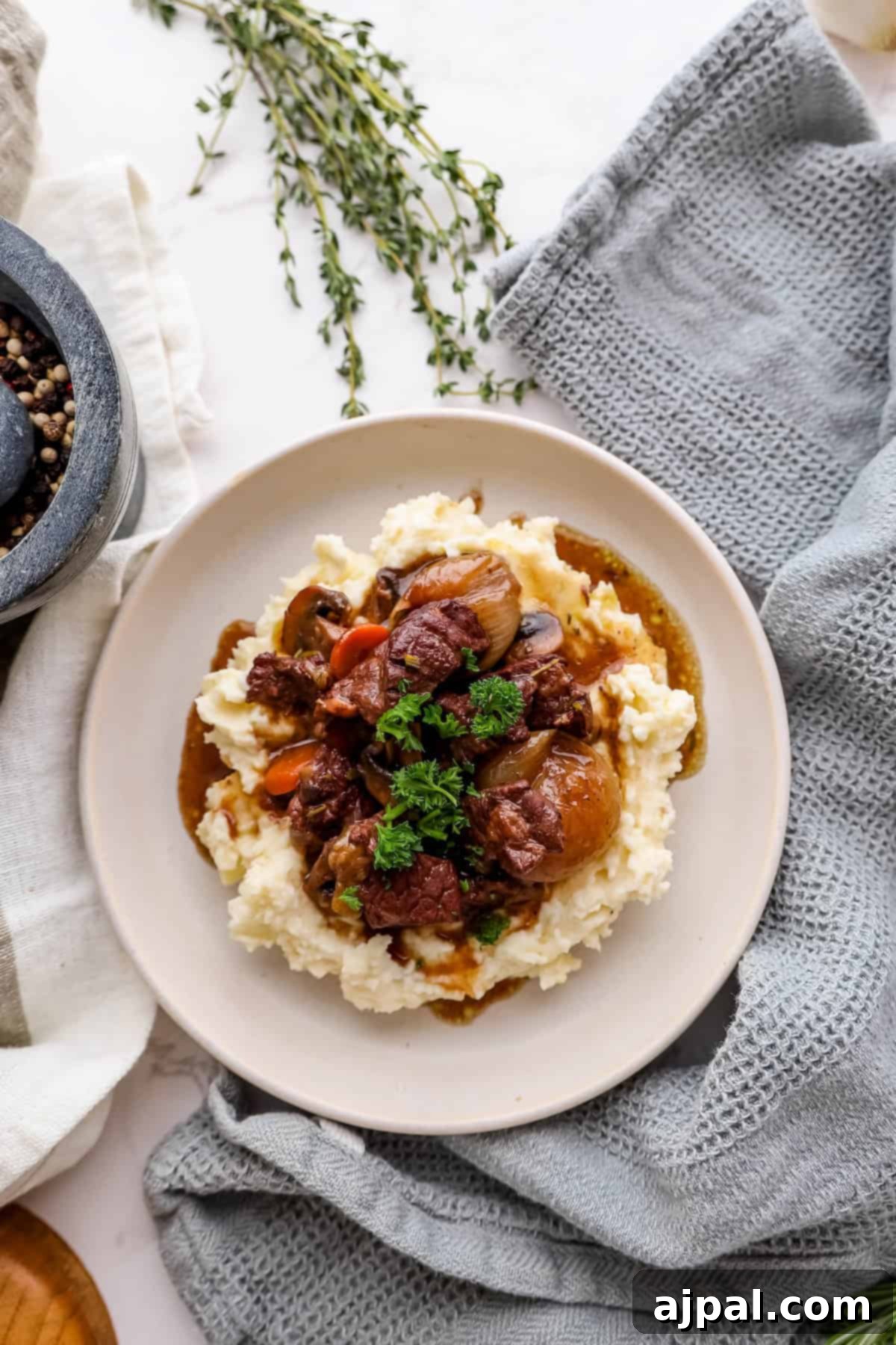 A generous serving of Beef Bourguignon and mashed potatoes, elegantly garnished with fresh herbs, nestled within a charming rustic table setting.