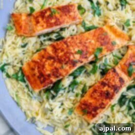 Three pieces of grilled salmon on a bed of orzo and spinach, served on a blue plate.