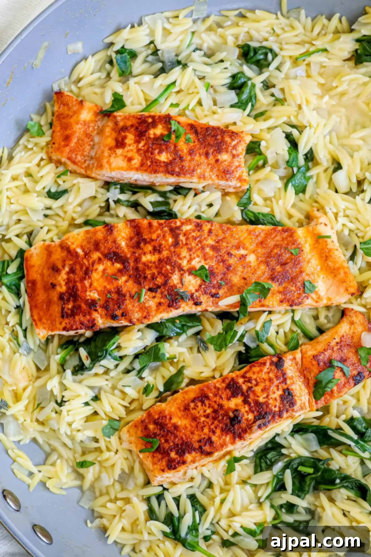 Creamy Salmon Florentine Orzo 4 Pan-seared salmon fillets on a bed of spinach and orzo pasta in a skillet.