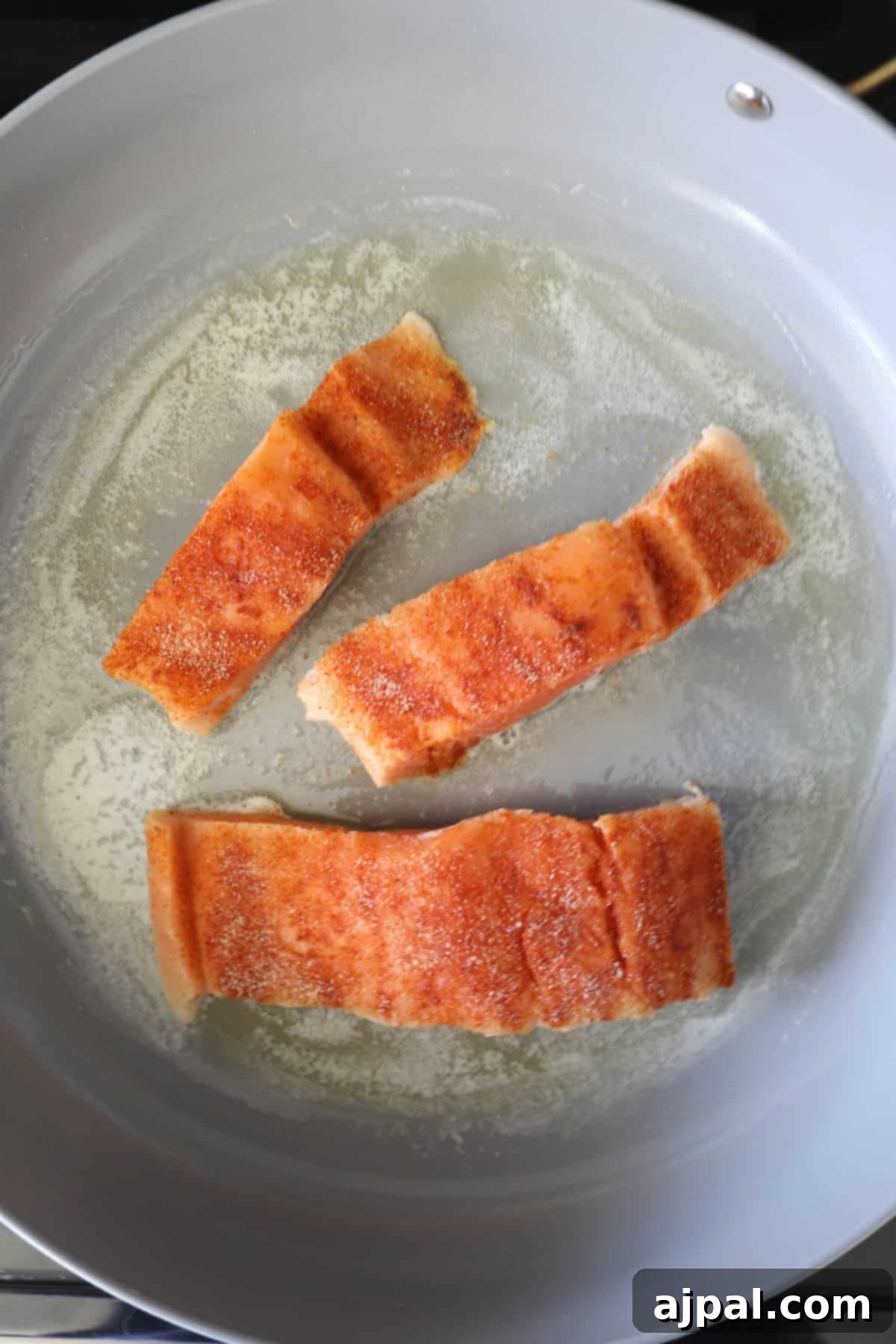Creamy Salmon Florentine Orzo 5 Three pieces of seasoned salmon frying in a skillet with melted butter.