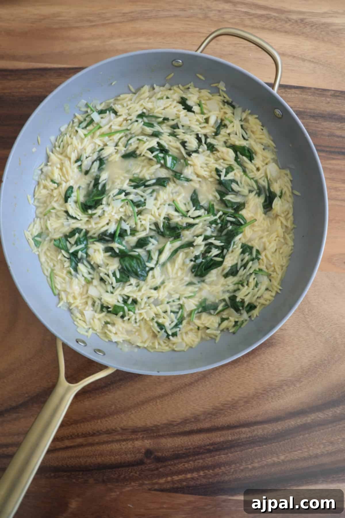 Creamy Salmon Florentine Orzo 9 A skillet with cooked orzo and spinach on a wooden surface.